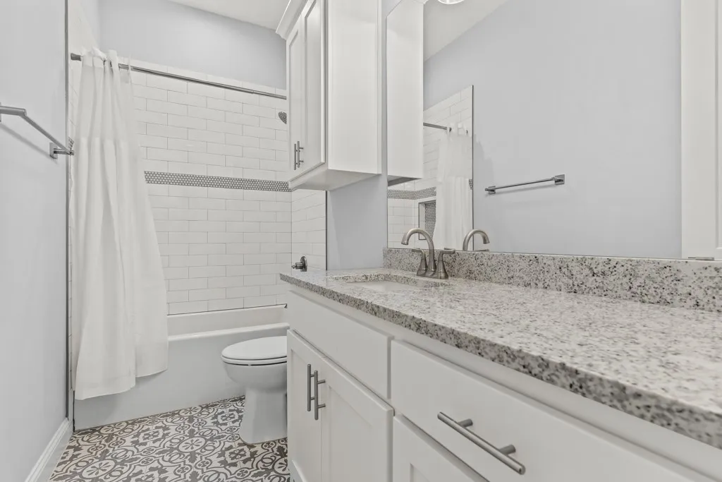 White subway tile shower surround with an accent band, white vanity cabinetry with brushed nickel hardware, and a light-toned speckled countertop