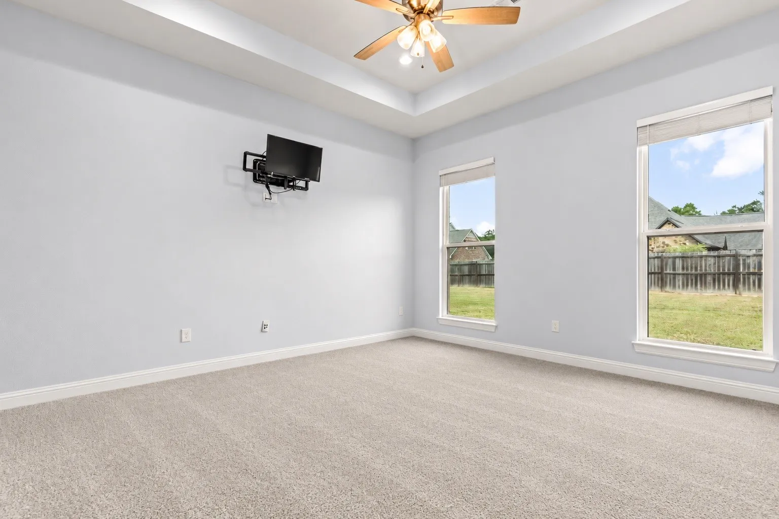Recessed tray ceiling with a built-in ceiling fan, two double-hung windows, and light-colored carpeting