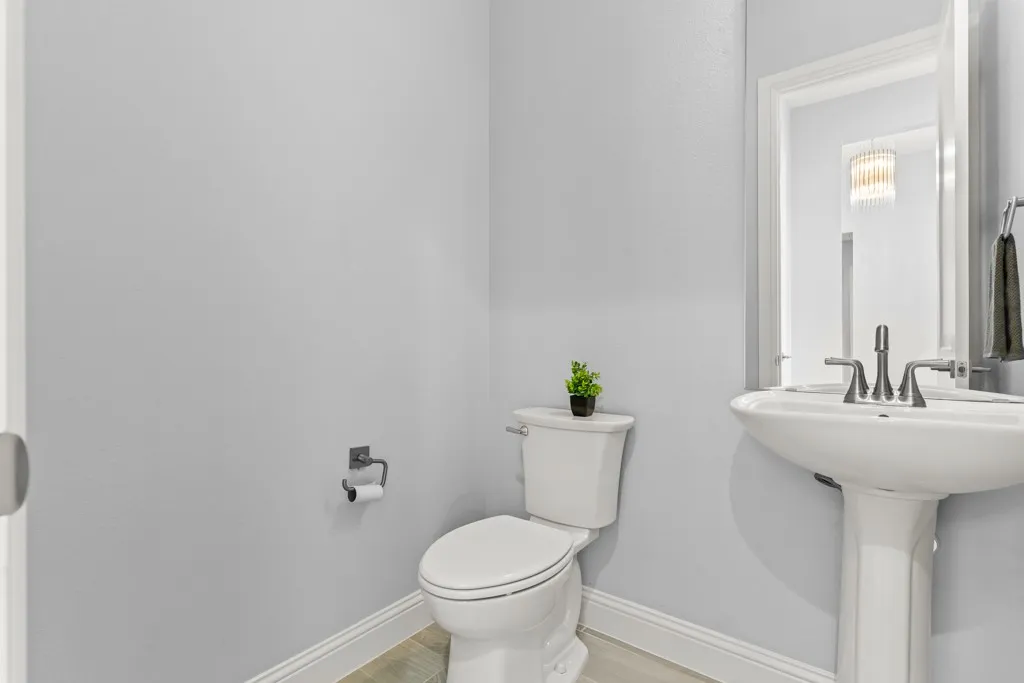 Pedestal sink with chrome-finish faucet, white toilet, and light-tone wood-finish flooring