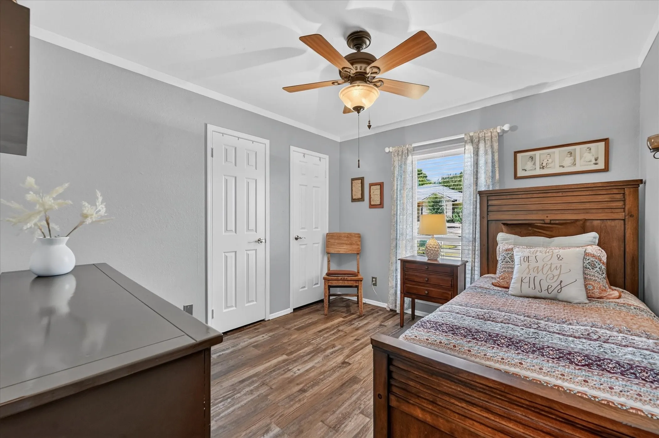 Comfortable secondary bedroom features wood-look flooring, a ceiling fan, crown molding, natural light, and convenient closet access.