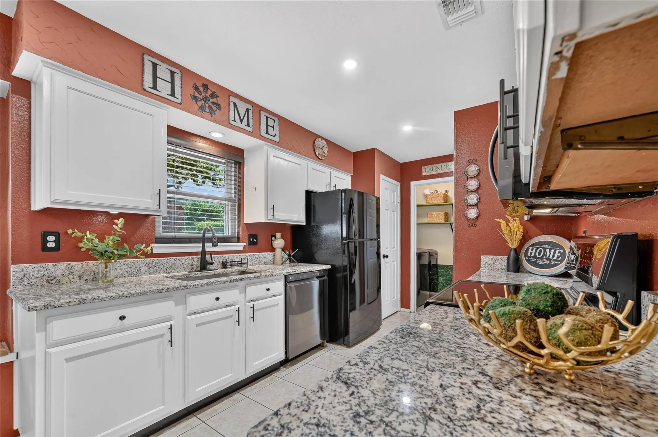 Bright kitchen showcases granite countertops, crisp white cabinetry, contrasting black hardware, and a window above the sink that brings in natural light.