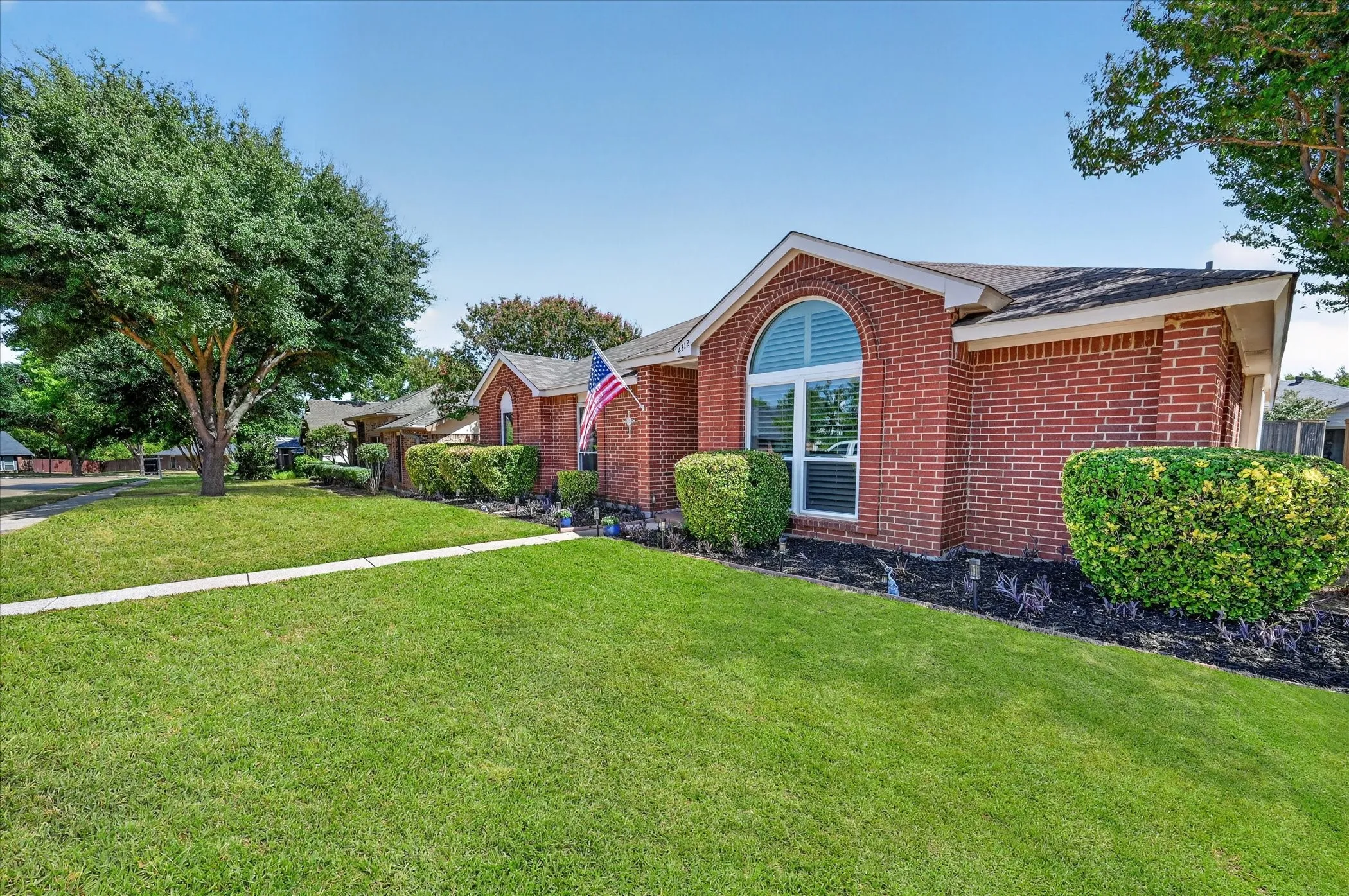 Classic red-brick architecture complemented by crisp white accents, manicured lawn, and beautifully maintained landscaping.