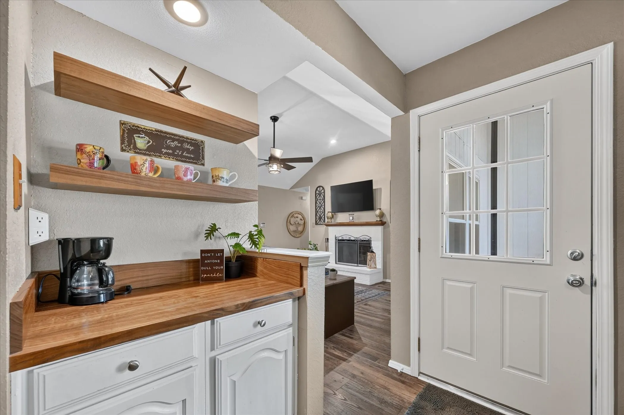 Charming beverage station features warm wood countertops, crisp white cabinetry, and floating shelves, adding both style and convenience between the office and living areas.
