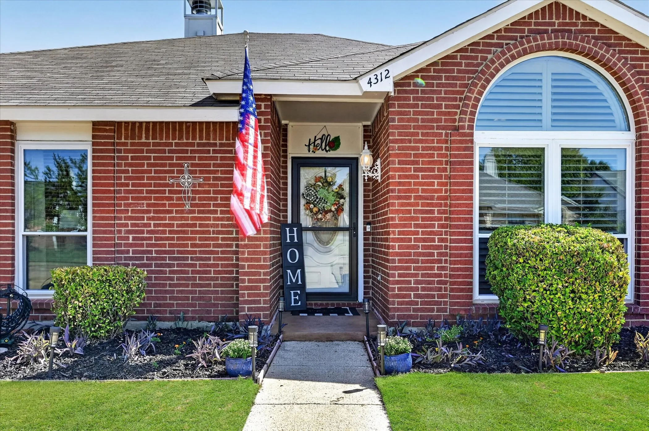 Welcoming covered entry highlighted by distinctive arched architectural details, lush landscaping, and a charming approach to the front door.
