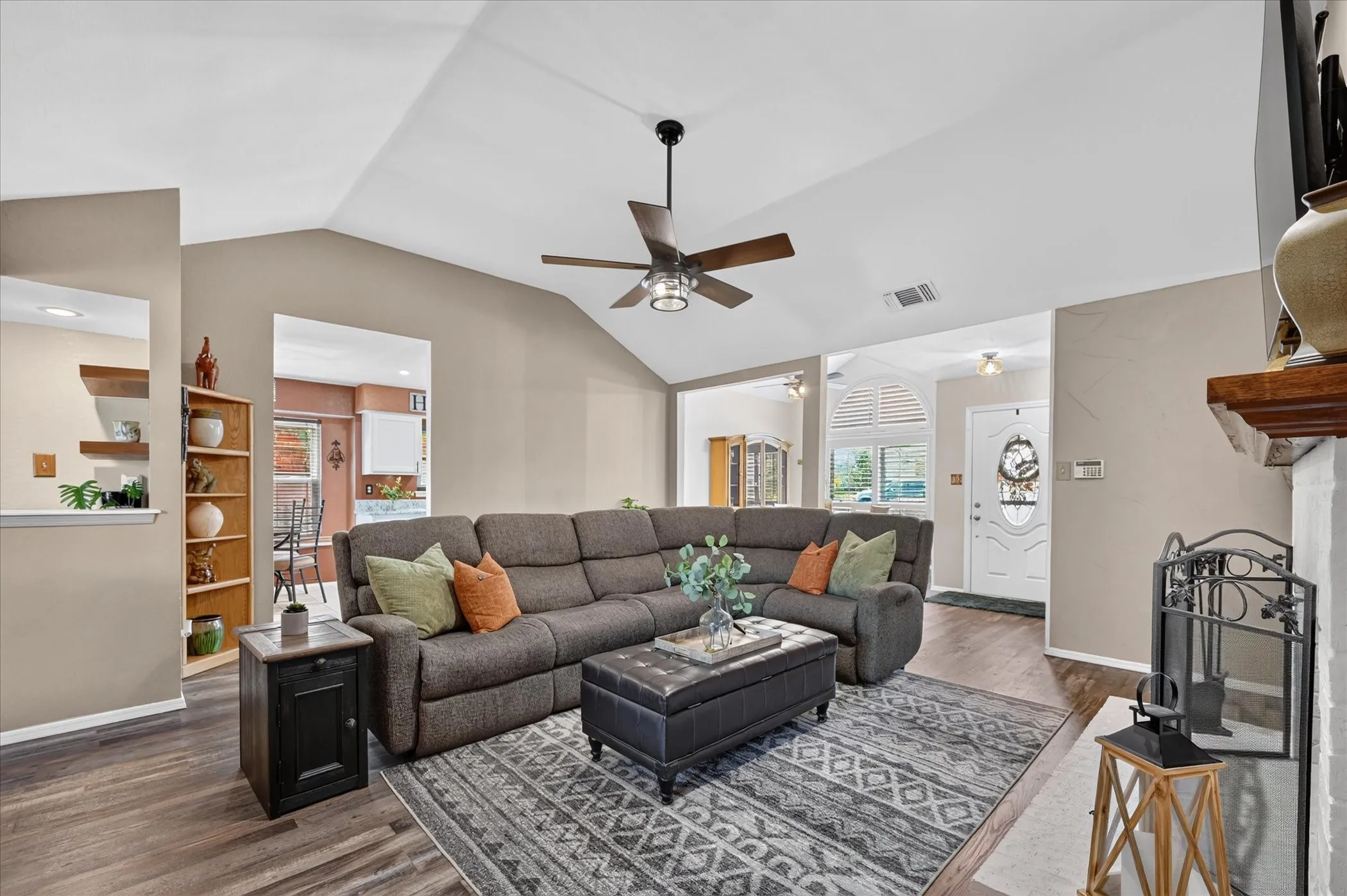 Inviting living room showcases a dramatic vaulted ceiling, rich wood-look flooring, and an open layout that flows effortlessly into the surrounding living spaces.