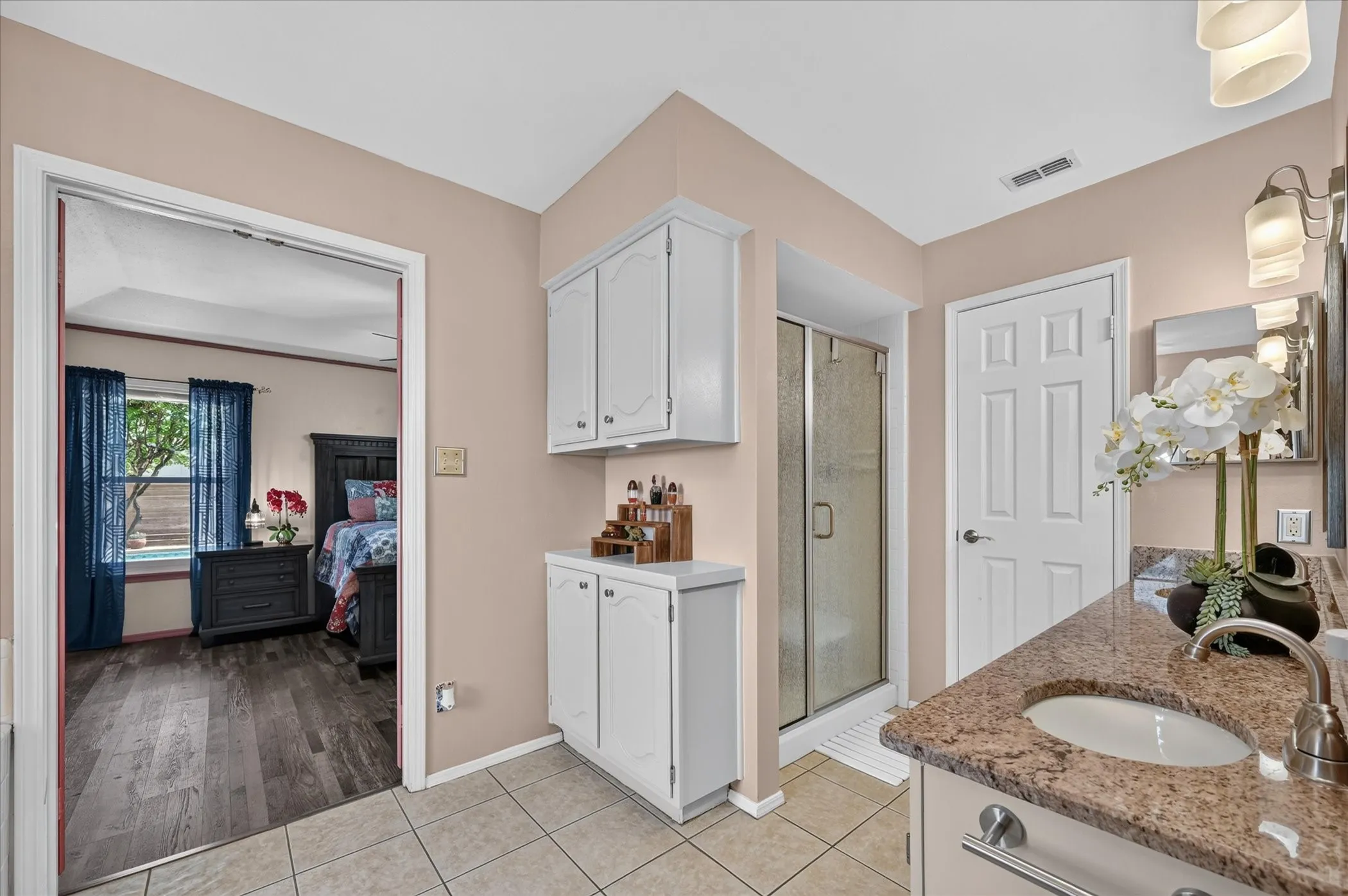 Primary bathroom offers a granite-topped vanity, additional built-in cabinetry, tile flooring, and a separate enclosed shower.
