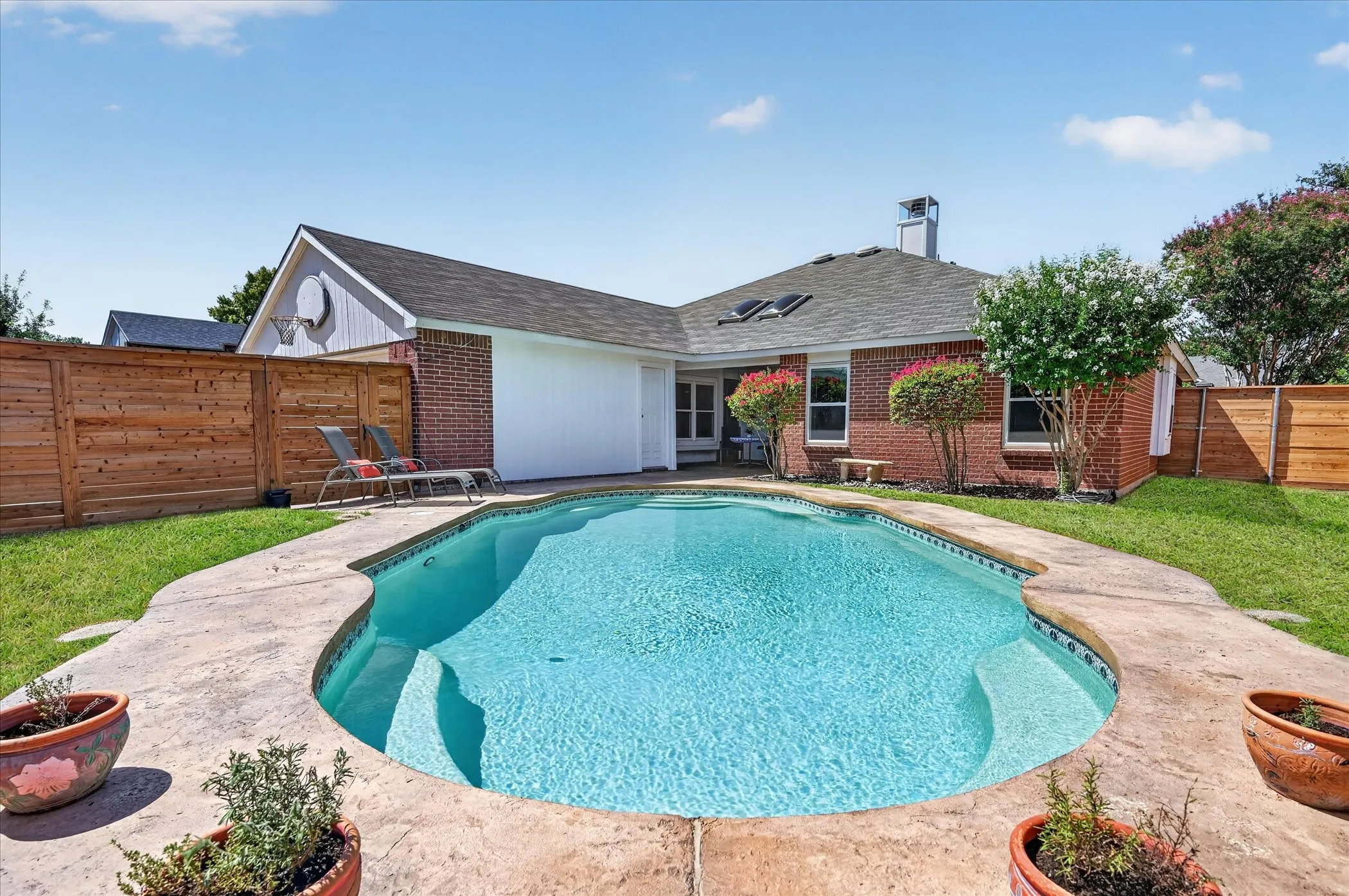 Private backyard retreat featuring a sparkling in-ground pool, generous poolside decking, mature landscaping, and a wood privacy fence.