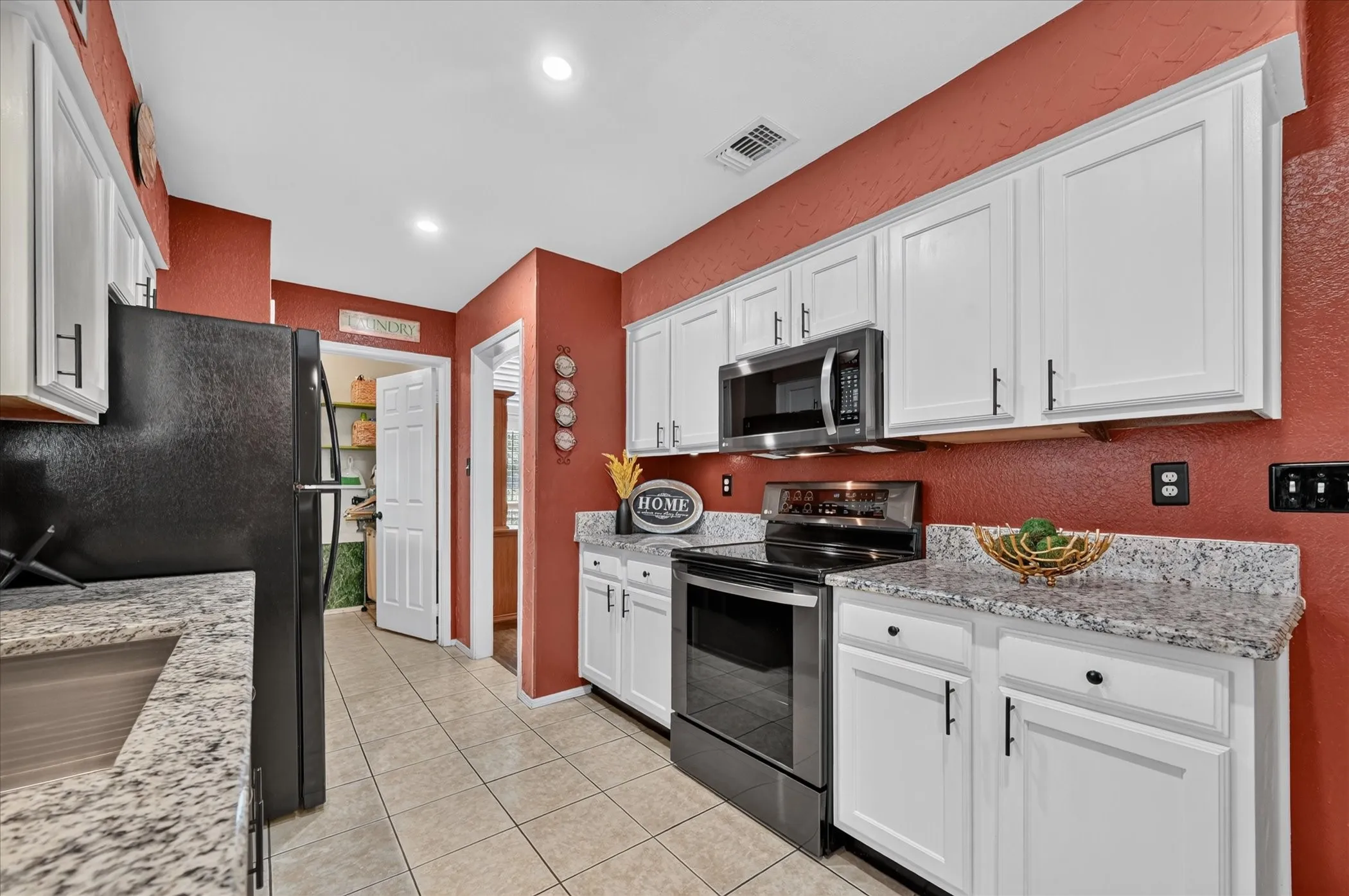 Polished kitchen features white cabinetry, granite countertops, sleek black appliances, contrasting hardware, and plentiful counter space for everyday meal preparation.