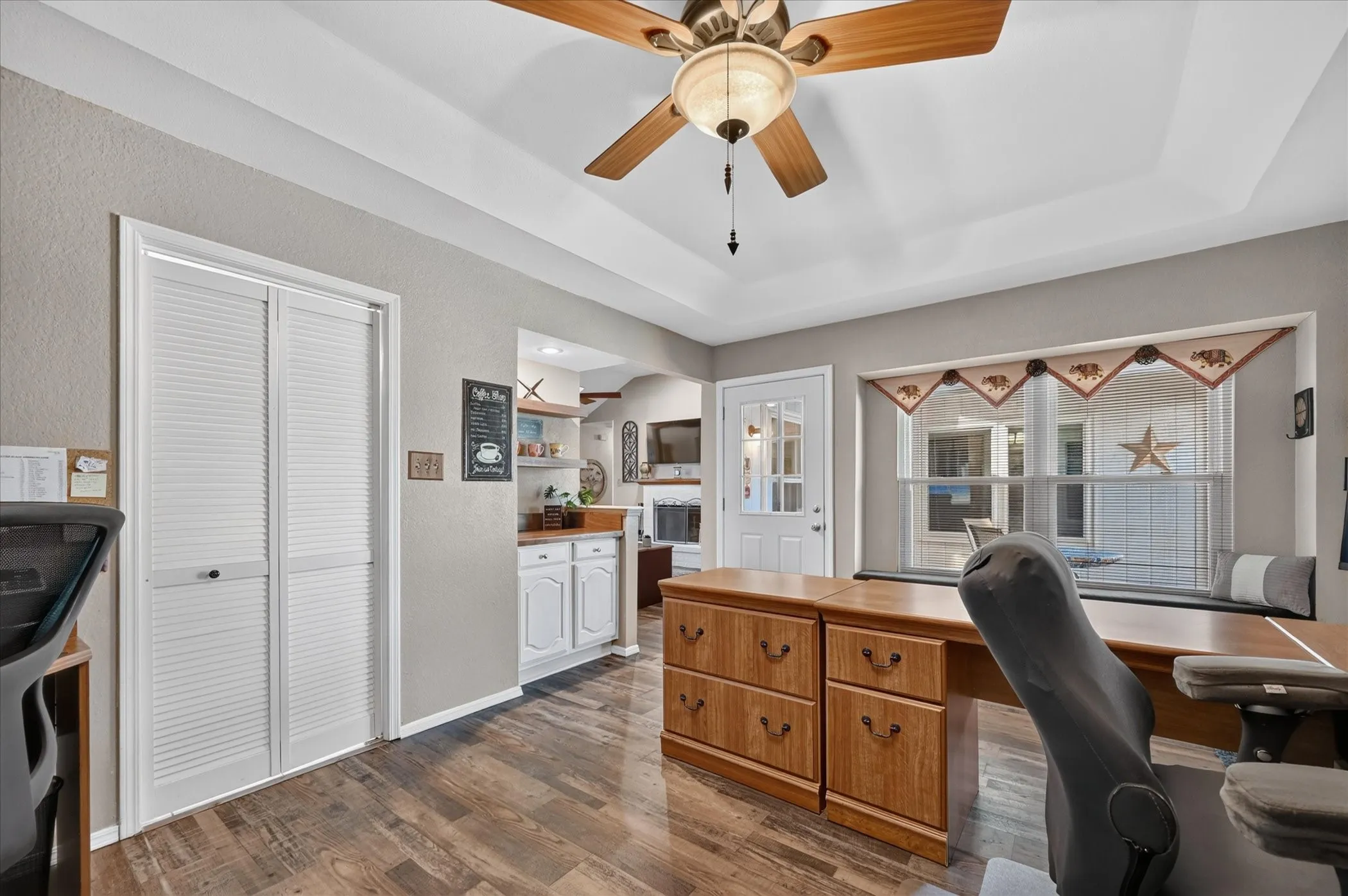 Light-filled workspace enhanced by a wide window with built-in seating, tray ceiling detail, and ample room for multiple workstations or a flexible bonus space.