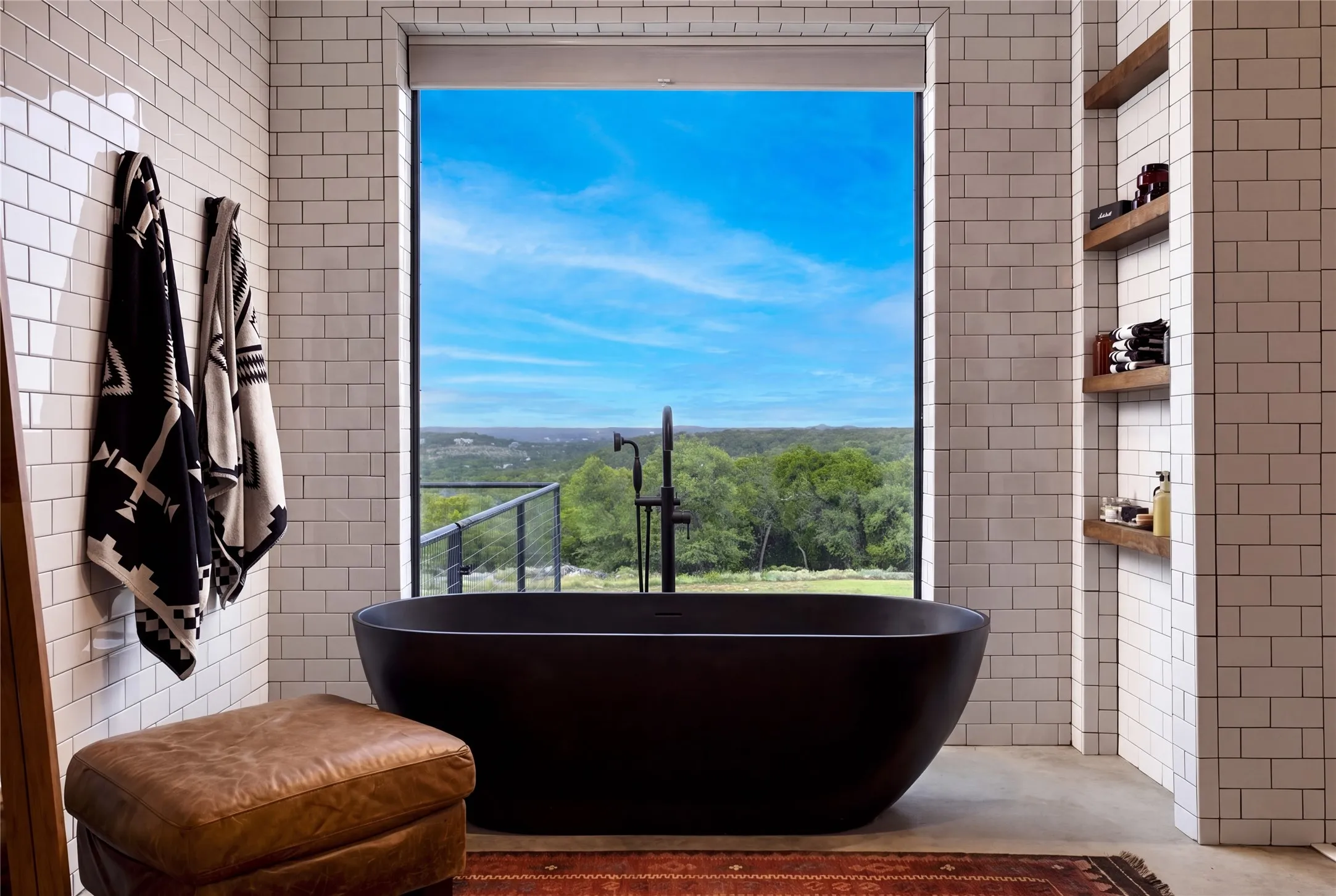 Floor-to-ceiling tiling frames a sleek soaking tub positioned before an expansive picture window offering views for miles of the iconic Texas hill country