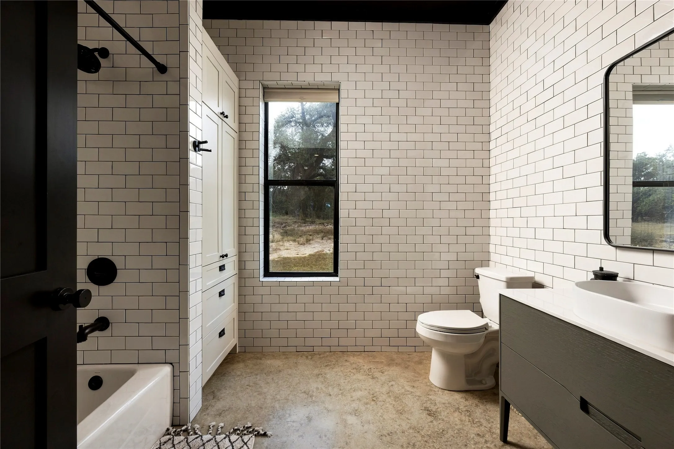 Classic subway tile wraps this modern bathroom featuring a sleek vanity and polished concrete flooring.
