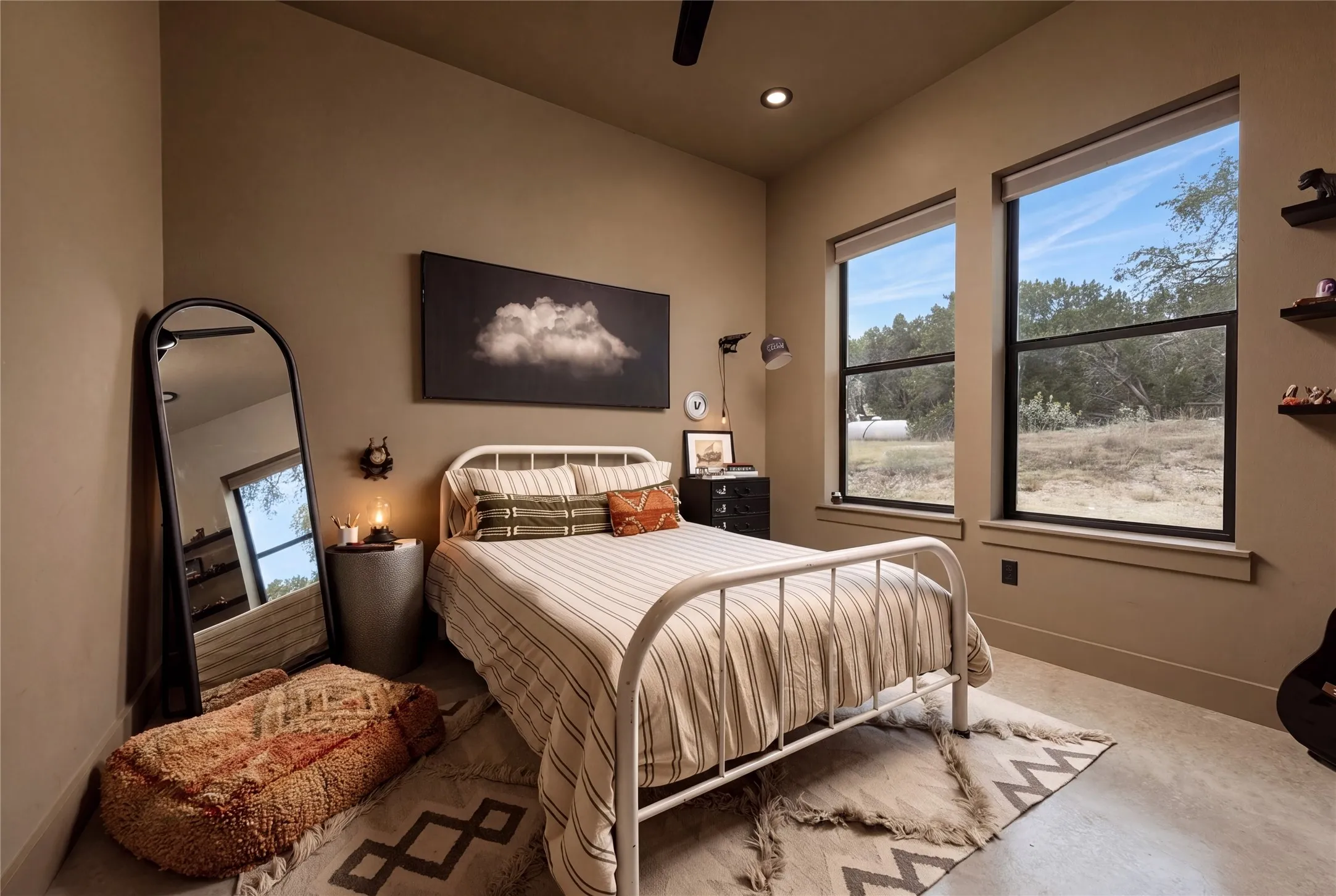 Stained concrete flooring and towering windows frame tranquil views in this light-filled bedroom.