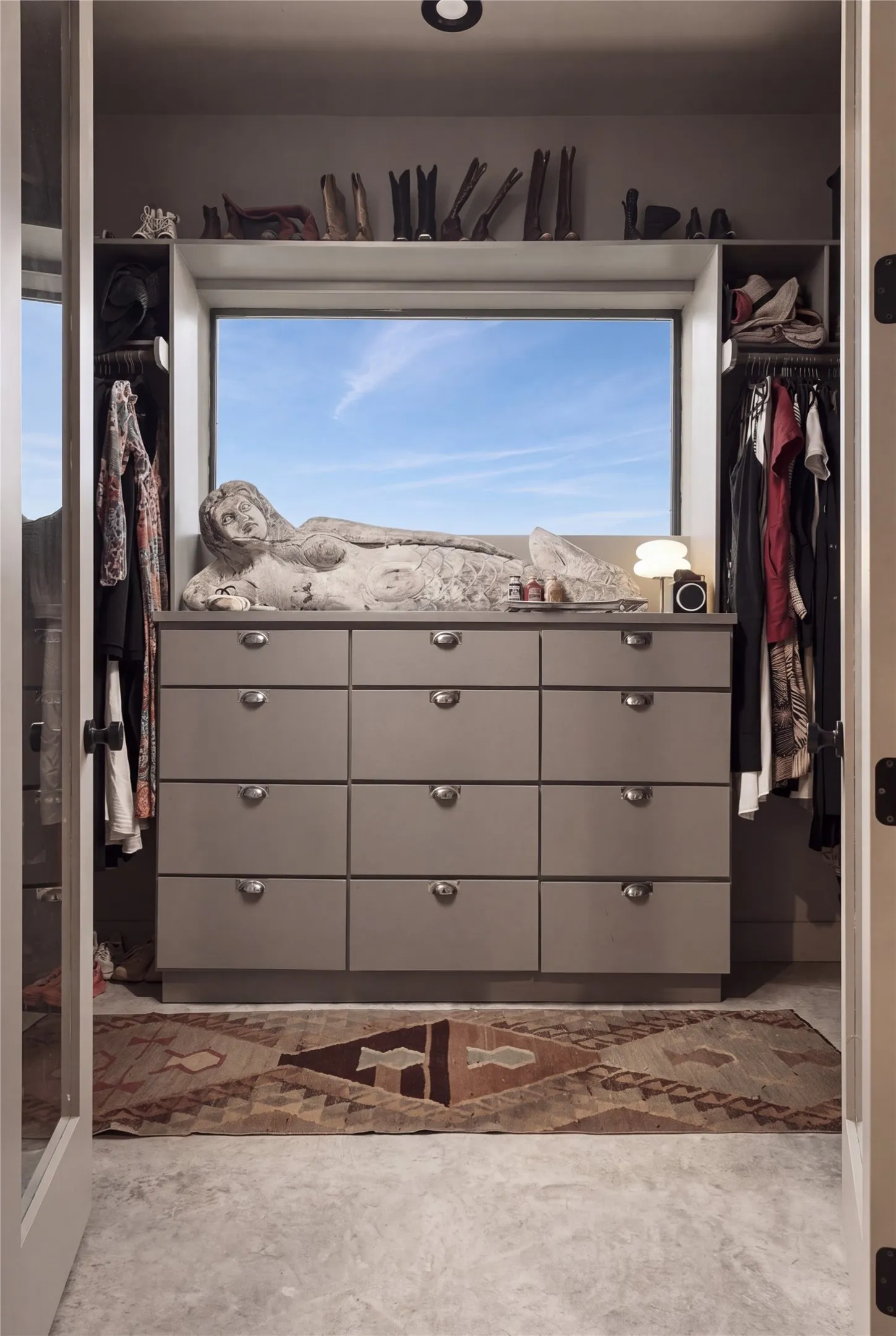 A spacious walk-in closet highlights custom built-in drawers beneath a picture window with sky views.