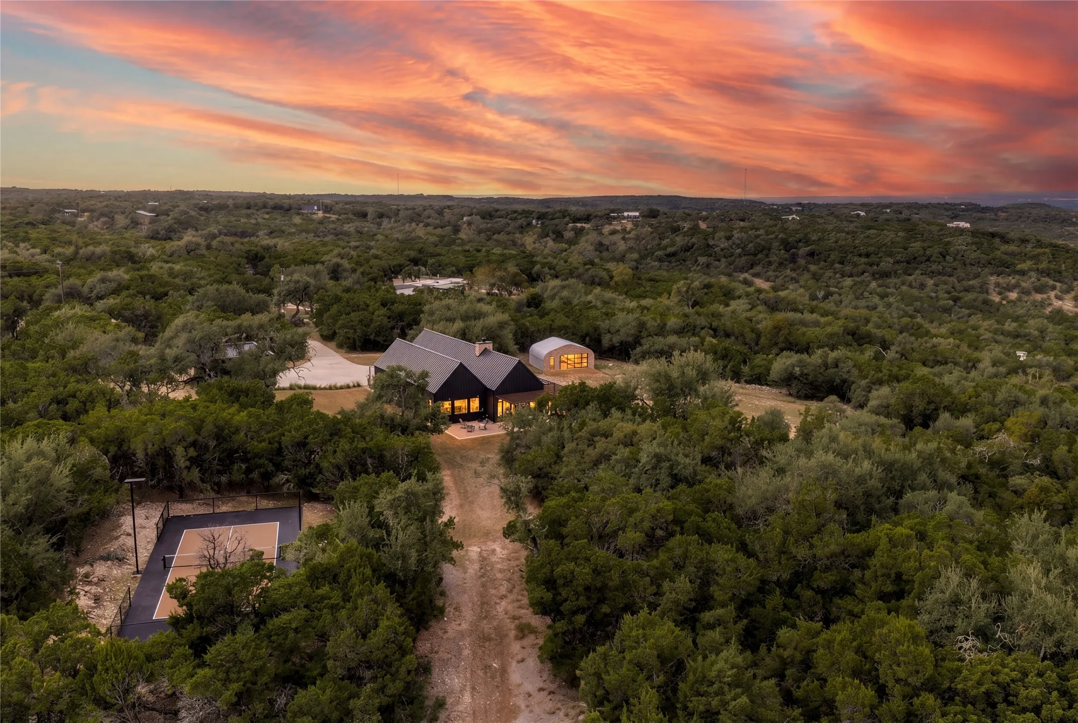 Thick woodlands envelop this secluded hill country estate under a colorful evening sky.