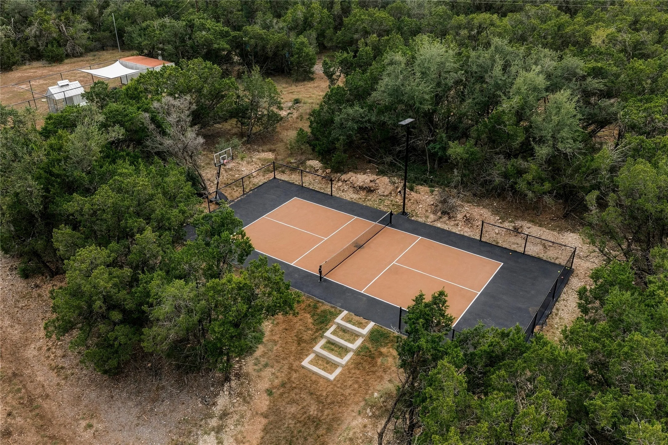 Mature trees surround a private, fenced pickleball and basketball court on this expansive property.