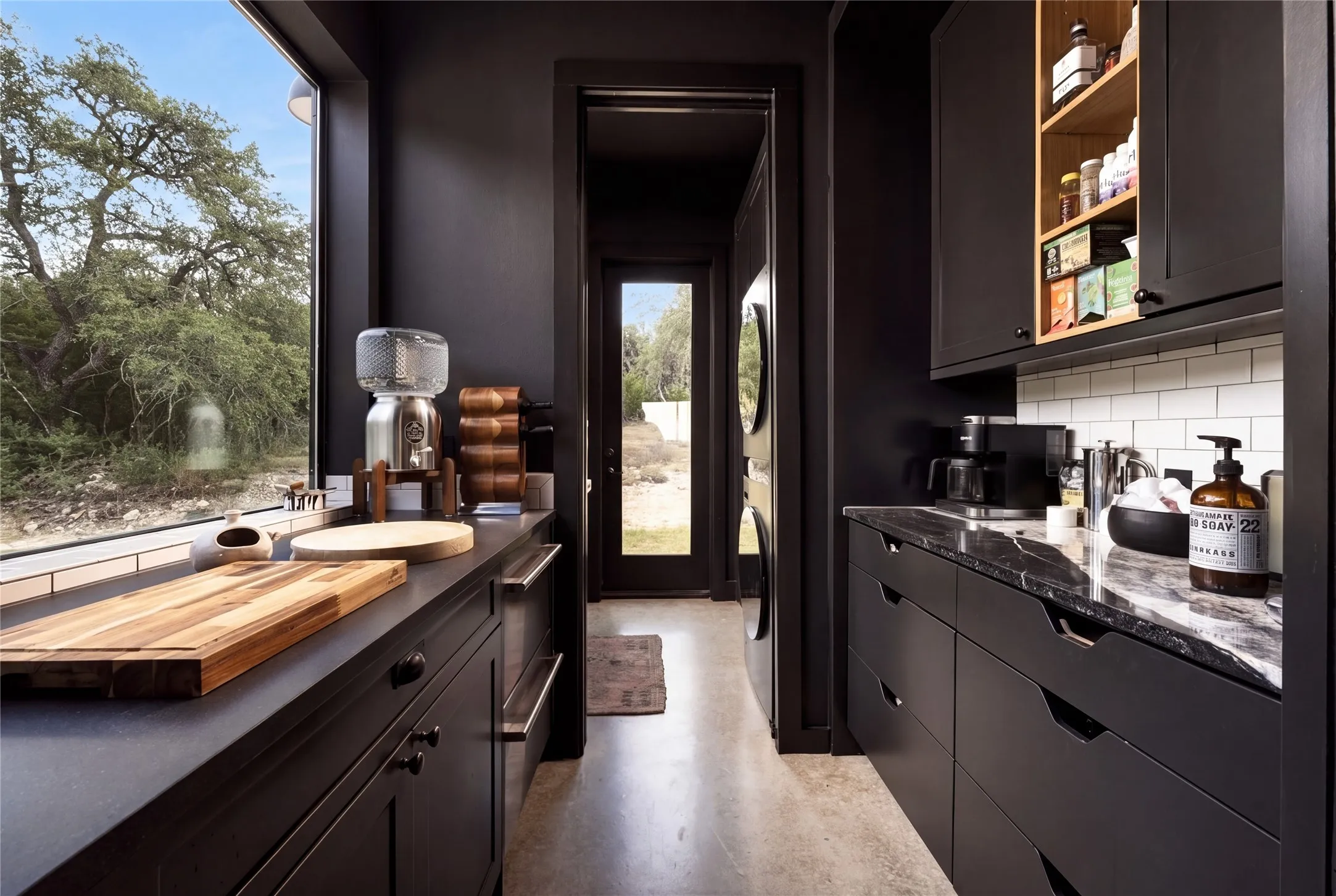 Polished concrete floors and dark cabinetry frame a large window looking out to nature.