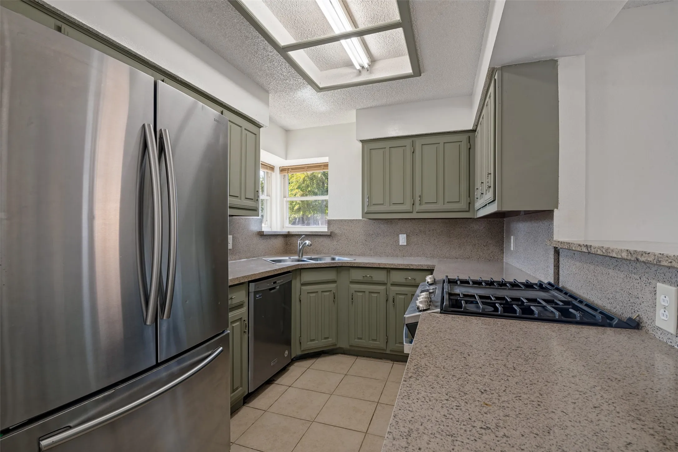 Kitchen featuring stainless steel refrigerator, built-in dishwasher, gas cooktop, and corner sink