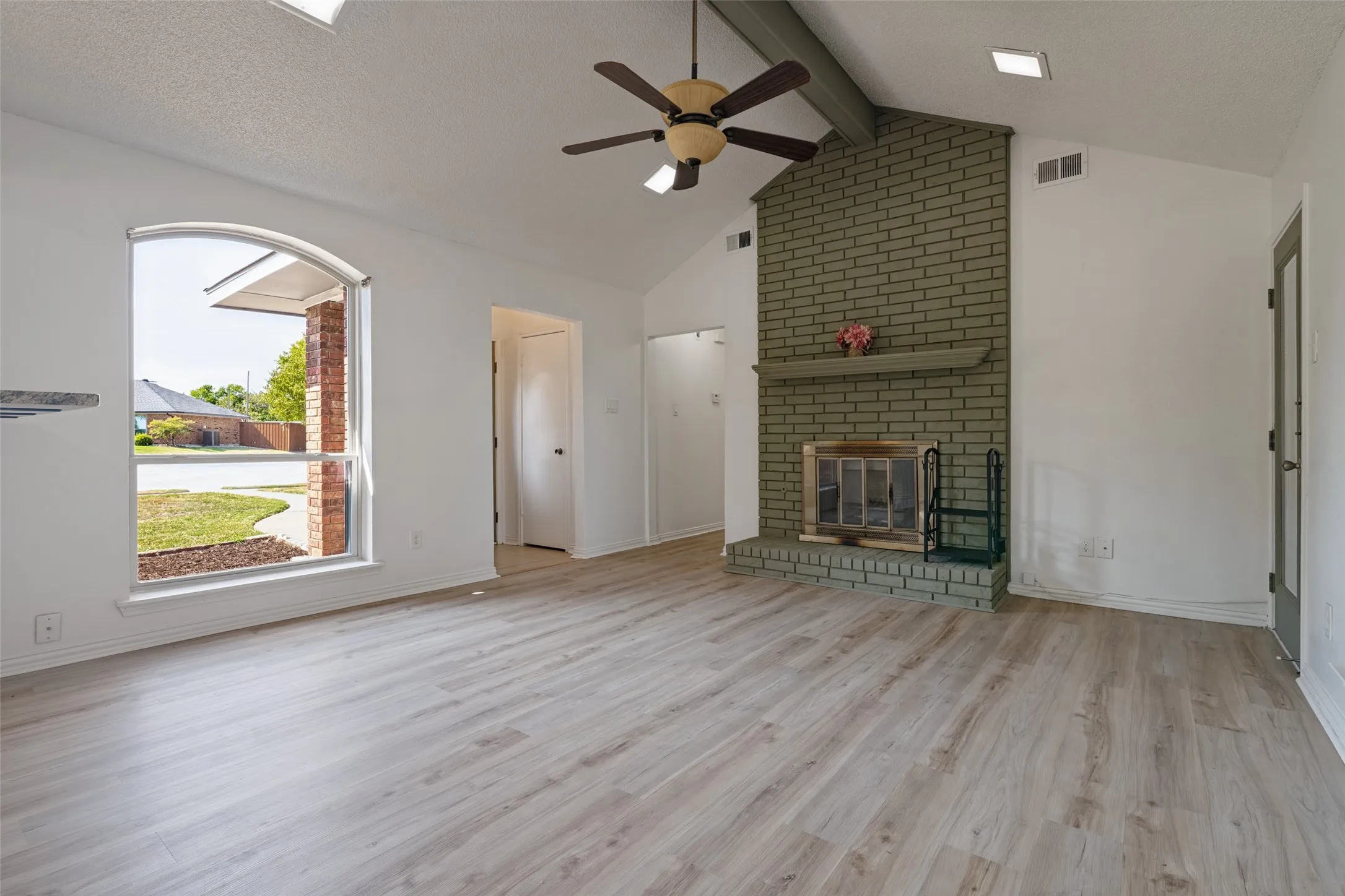 Vaulted ceiling, ceiling fan, brick fireplace, wood-finish flooring, and arched window.