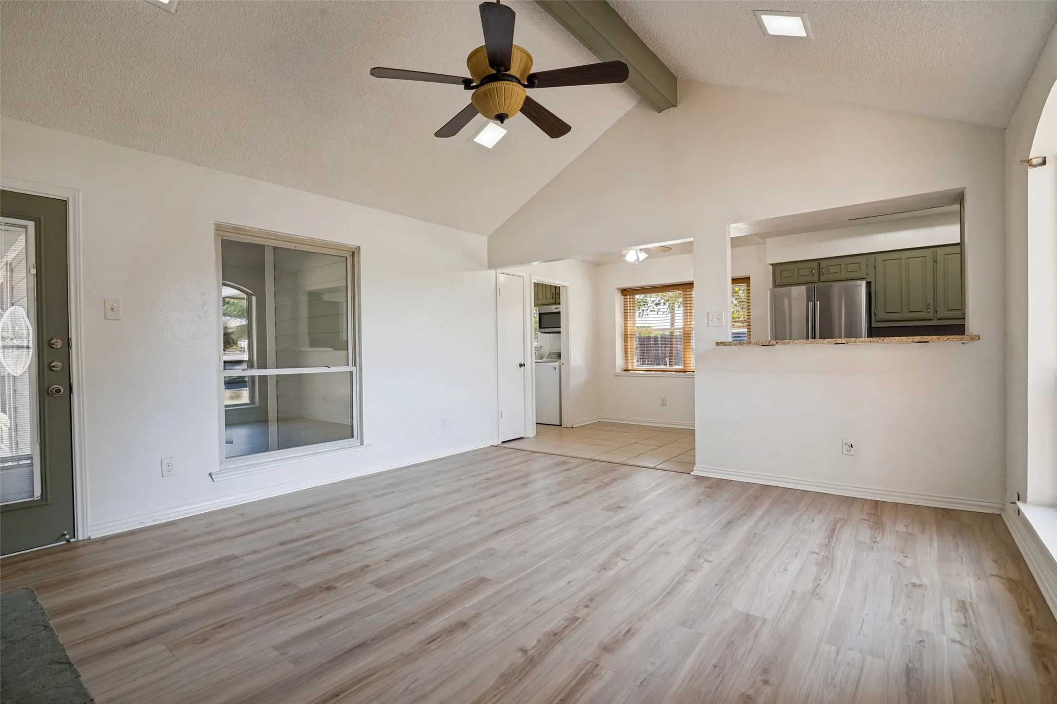 Vaulted ceiling with exposed beam, wood-finish flooring, ceiling fan, breakfast bar pass-through window to the kitchen.