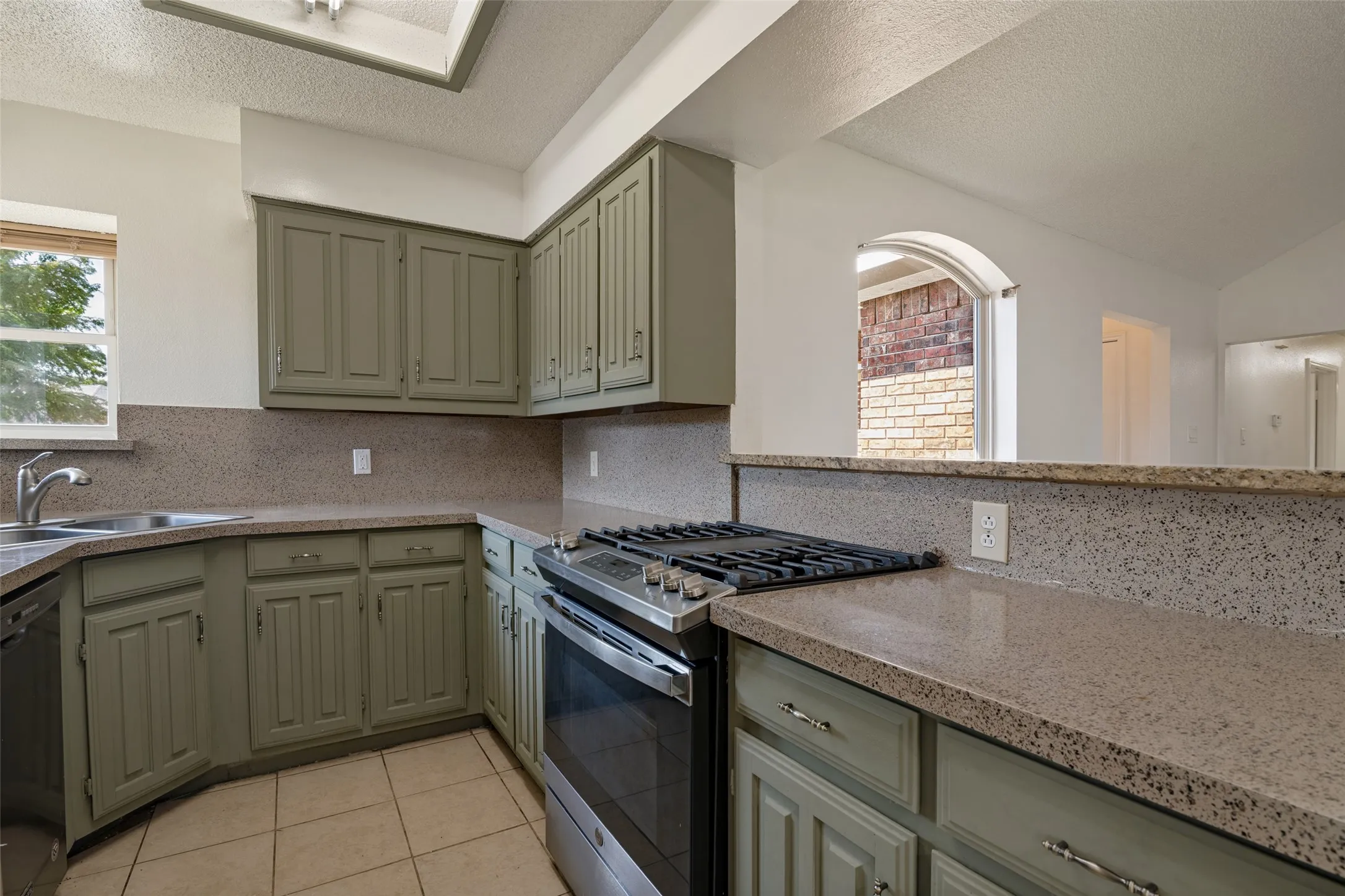 Kitchen featuring light green cabinetry, integrated stainless steel oven with gas cooktop, L-shaped countertop, and tile flooring