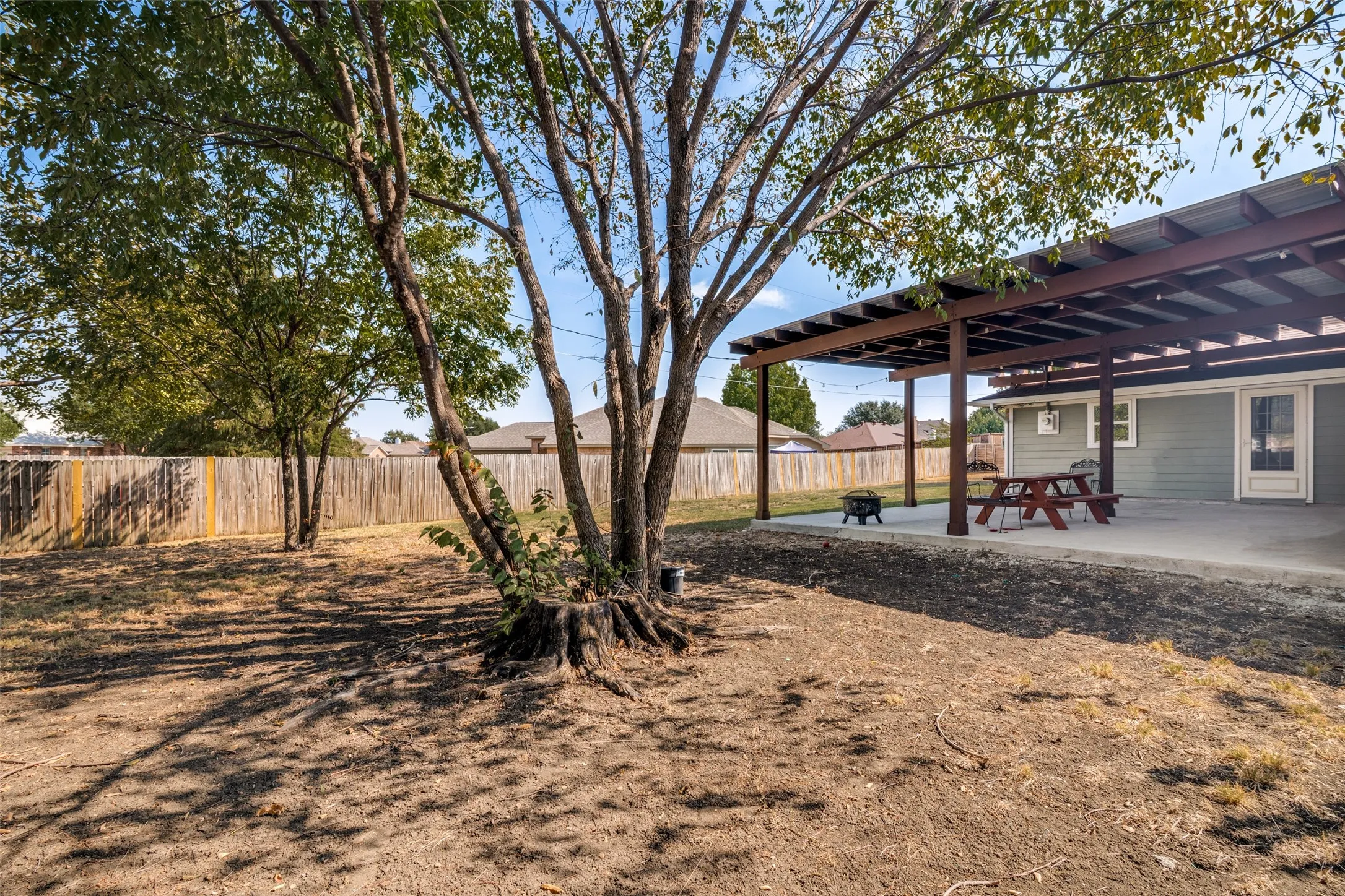 Expansive backyard featuring a concrete covered patio, privacy fencing, and mature trees.