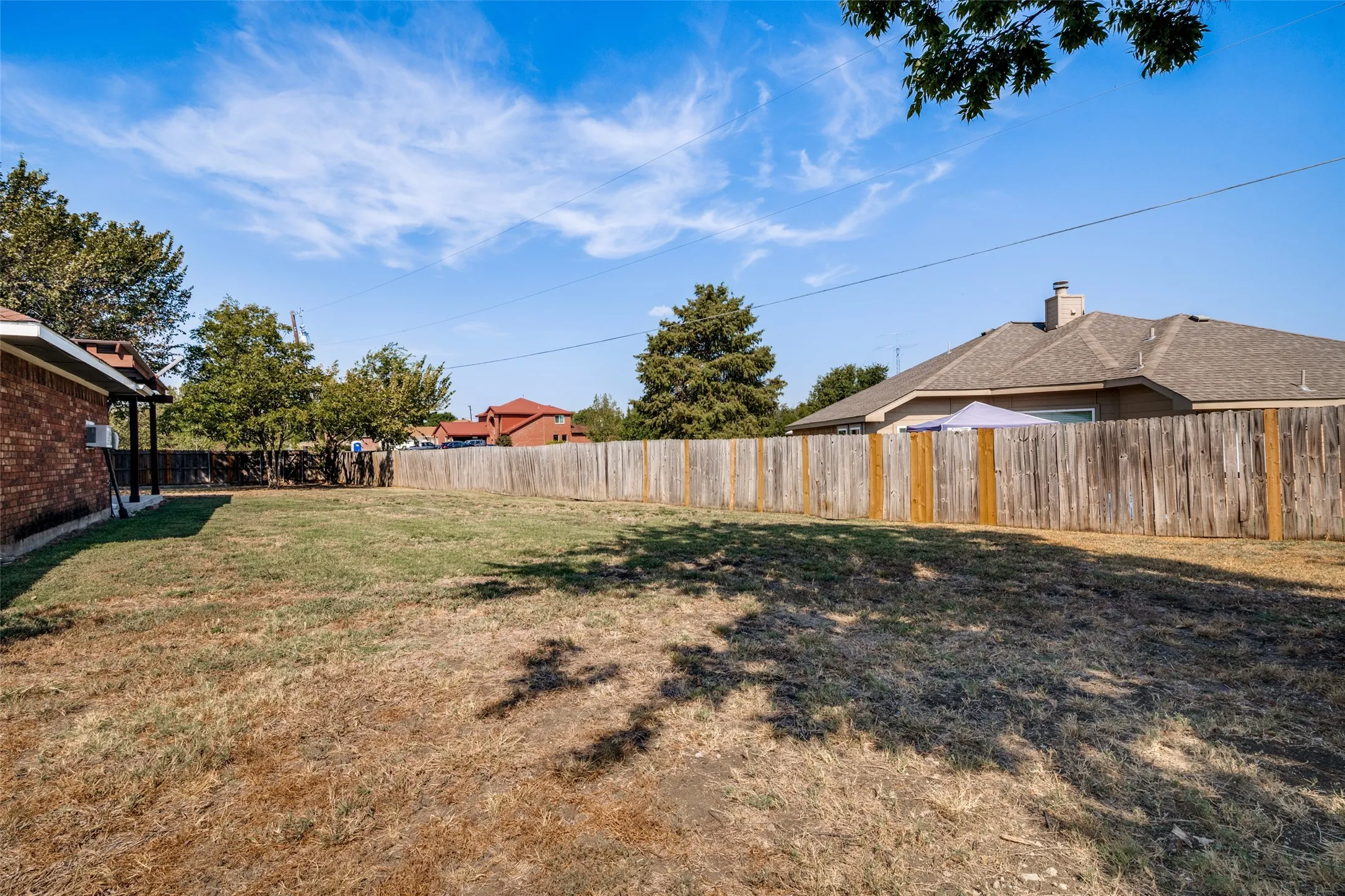 Spacious backyard area featuring a wooden privacy fence, and mature trees.