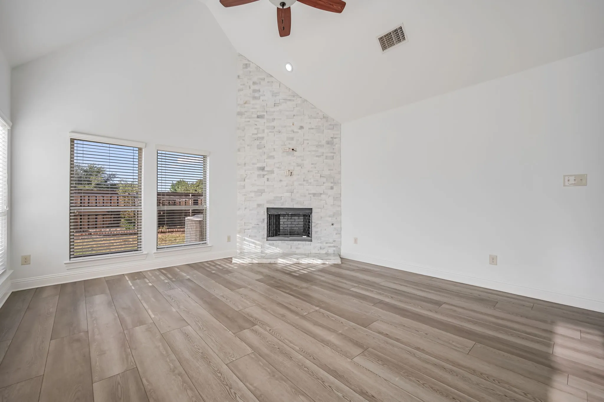 Vaulted ceiling with a ceiling fan, a tiled fireplace, wood-finish flooring, and multiple windows