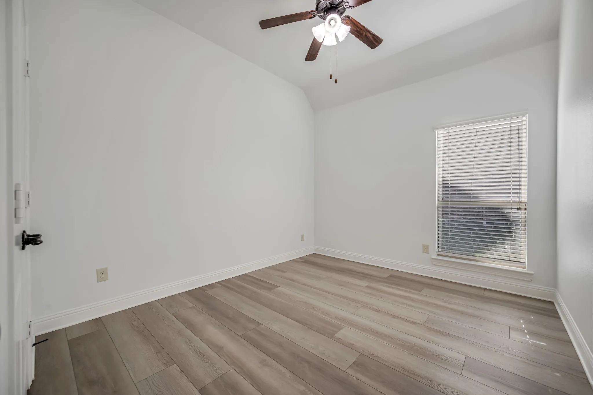Wood-finish flooring, white painted walls, window with blinds, ceiling fan with light fixture, and white trim