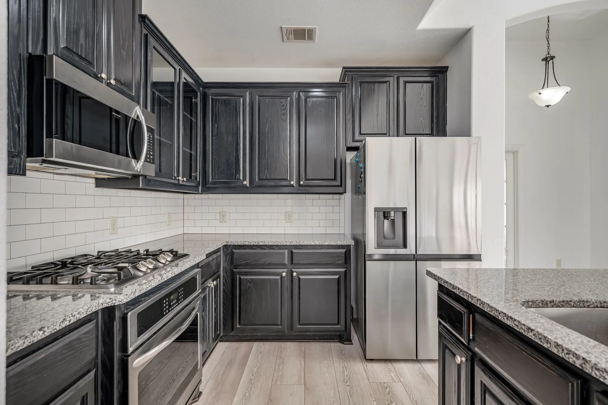 Kitchen featuring dark wood cabinetry, granite countertops, white subway tile backsplash, stainless steel appliances, and wood-finish flooring