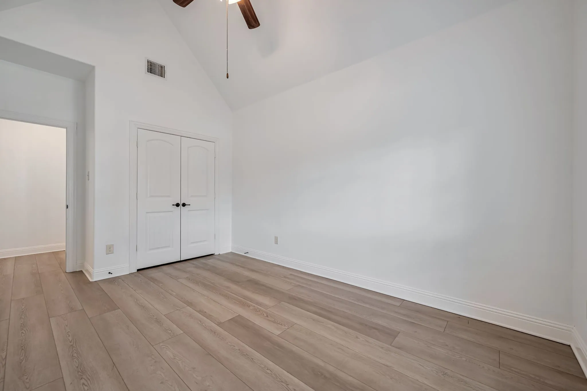Vaulted ceiling, wood-finish flooring, white walls, double bi-fold doors, and a ceiling fan