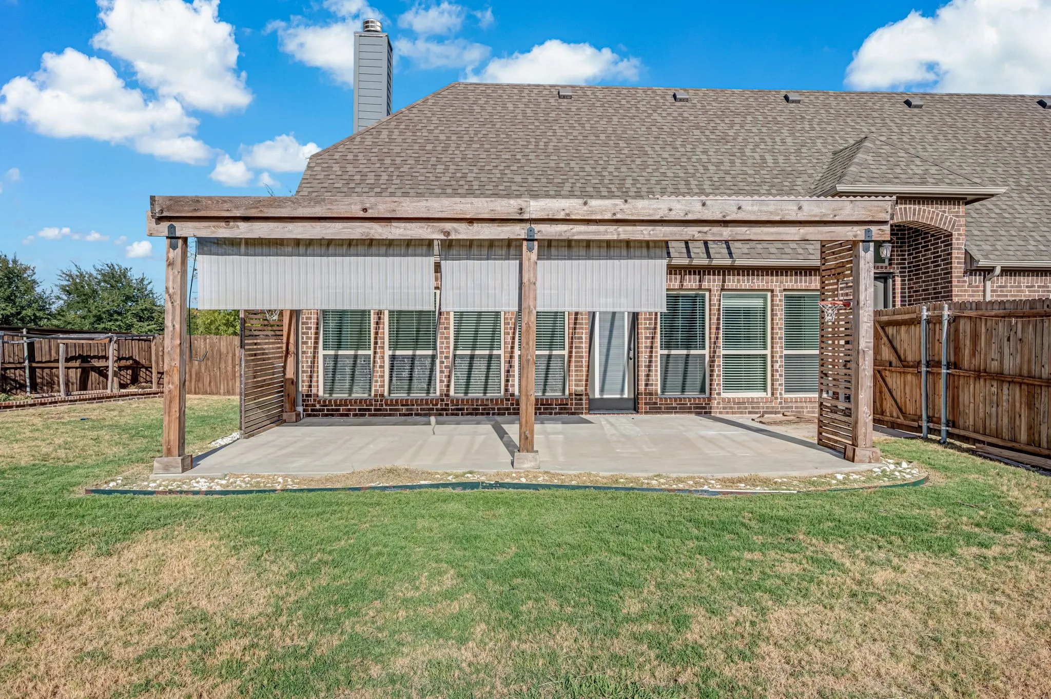 Paved patio with a wood pergola, integrated shades, and a brick exterior