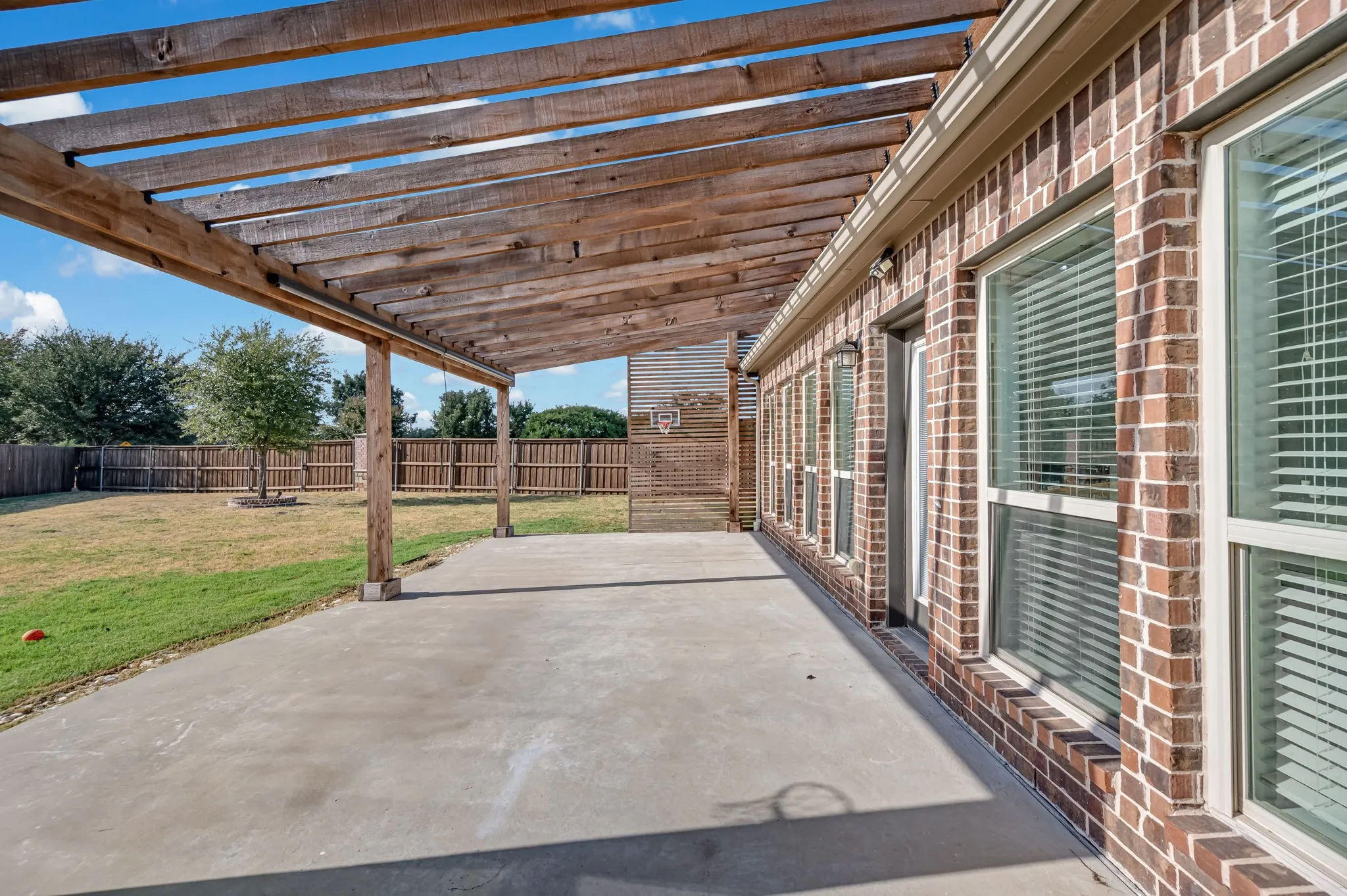 Expansive concrete patio with a wooden pergola, brick exterior, and multiple windows