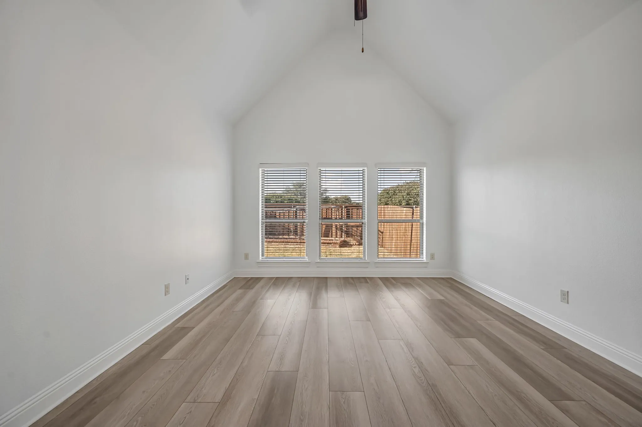 Vaulted ceiling with a ceiling fan, three large windows with blinds, and wood-finish flooring