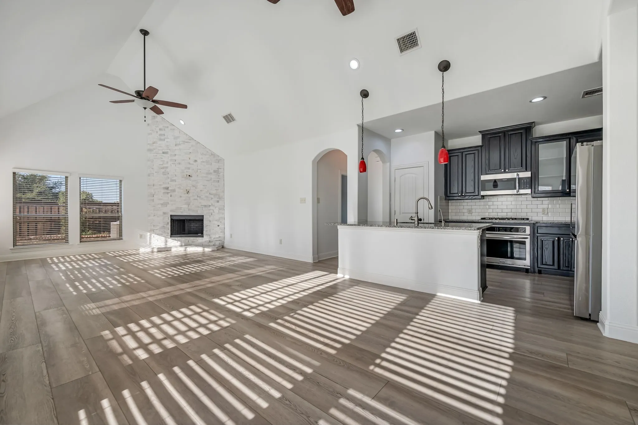 Vaulted ceiling with wood-finish flooring, stone fireplace, and a kitchen island with pendant lighting