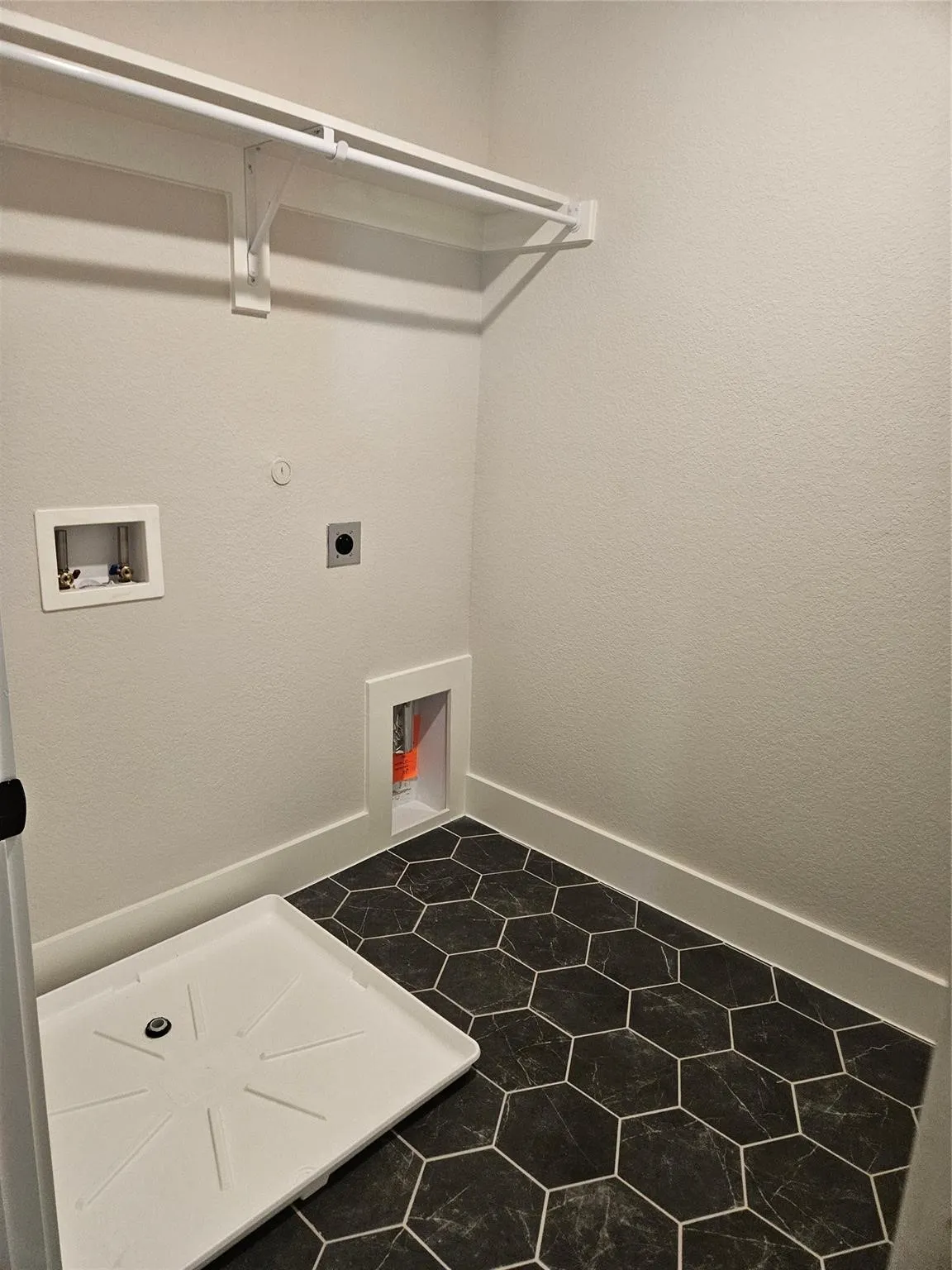 White shelf and hanging rod, textured white walls, utility hookups, and hexagonal floor tiling