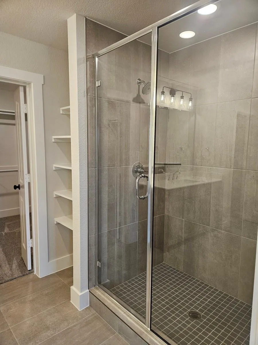 Frameless glass shower enclosure with a rainfall showerhead, recessed lighting, and wall-mounted shelving