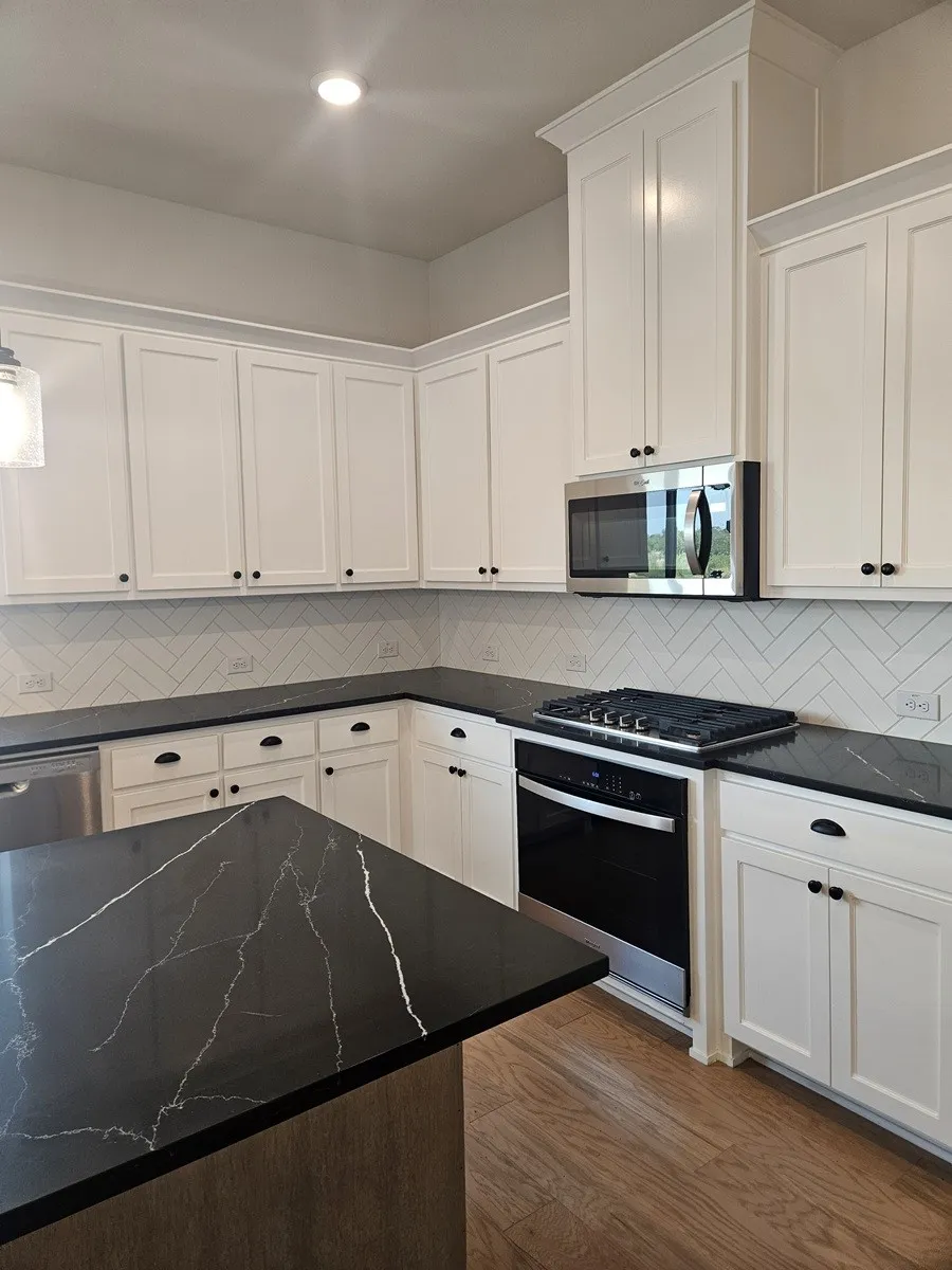 White shaker cabinetry, dark countertops with light veining, stainless steel appliances, herringbone tile backsplash, and wood-finish flooring