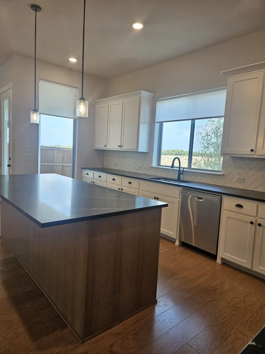 Kitchen featuring an expansive island with a dark countertop, stainless steel dishwasher, white shaker-style cabinetry, and wood-finish flooring