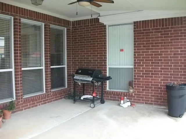 Covered patio with brick exterior, concrete flooring, and ceiling fan