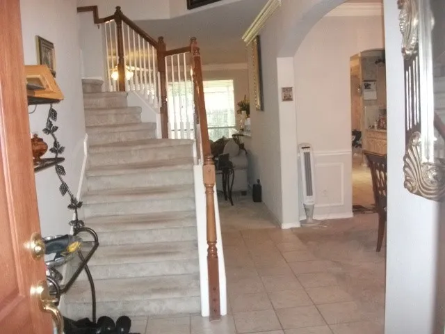 Staircase with wood and white baluster railing, archway entry, wainscoting, and tile flooring