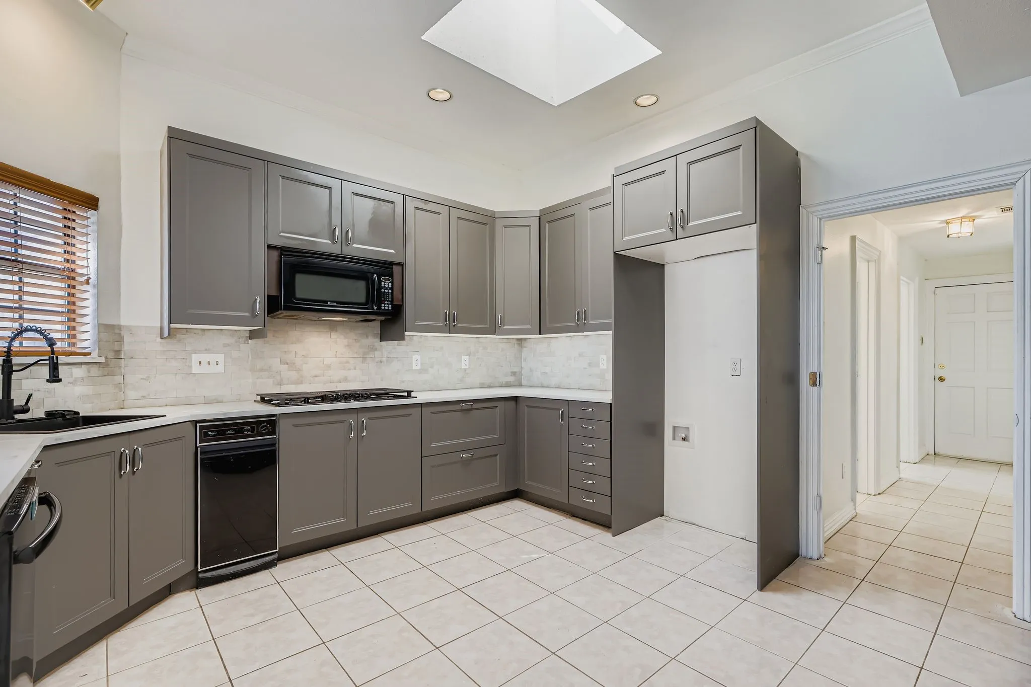 Kitchen featuring gray cabinetry, light-toned backsplash, white countertops, and a skylight