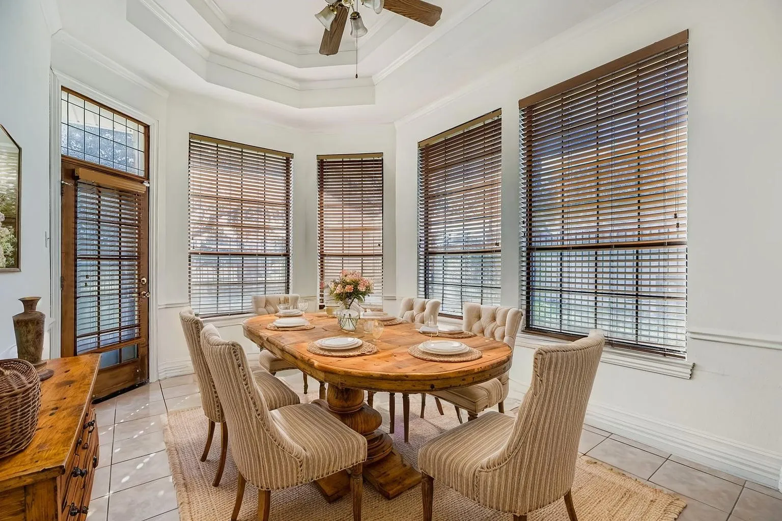 Bay window with multiple large windows, tile flooring, a tray ceiling, and a ceiling fan