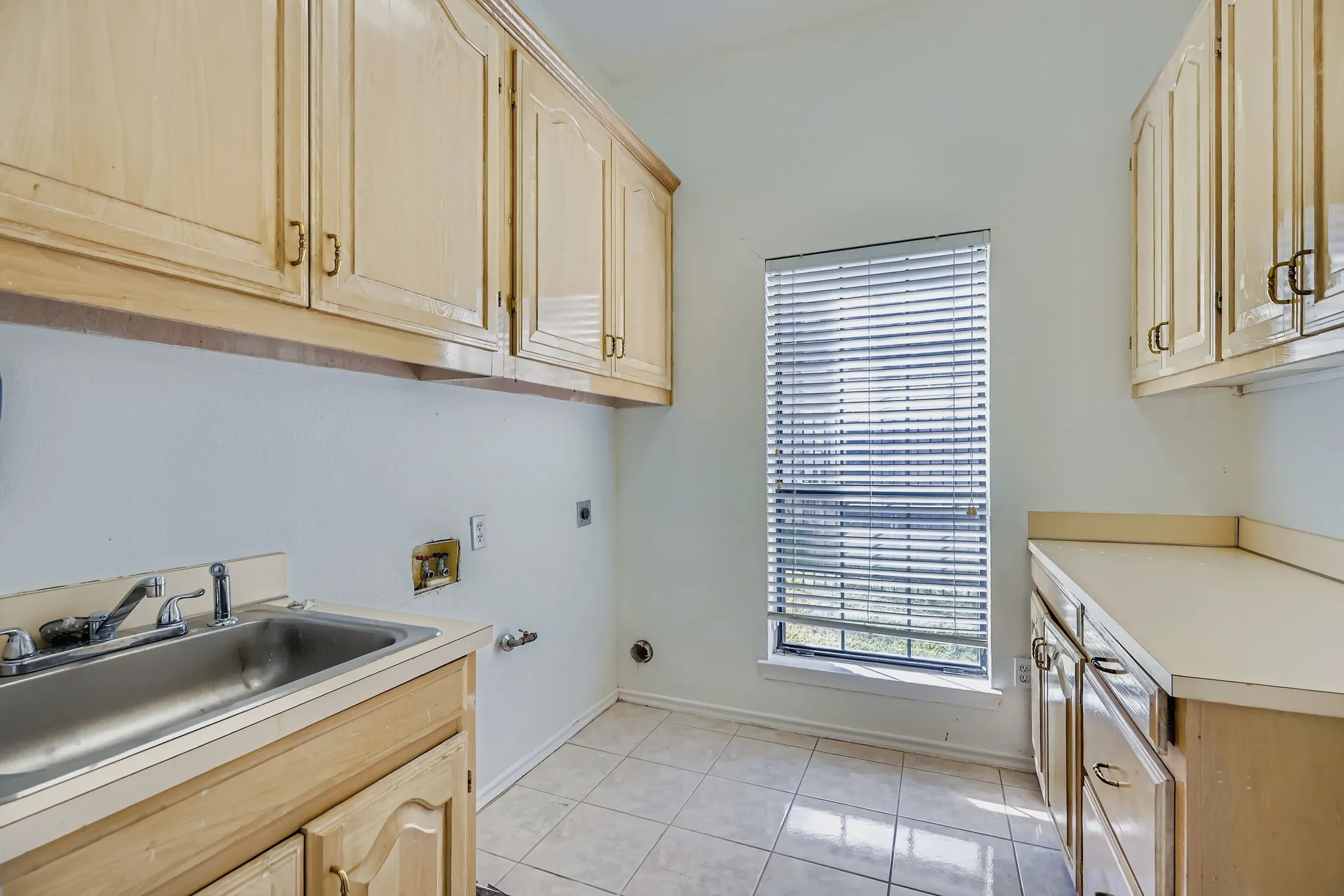 Full-height upper cabinetry, a stainless steel utility sink, and a window with horizontal blinds