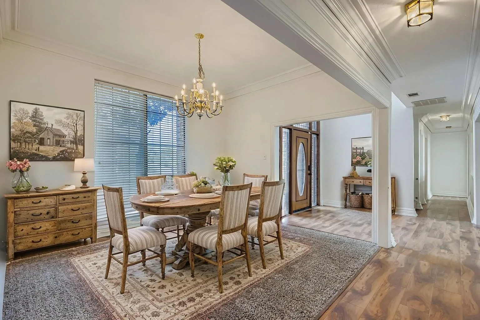 Recessed wood-finish flooring, decorative chandelier, transom window with blinds, and a paneled entry door with an oval glass insert