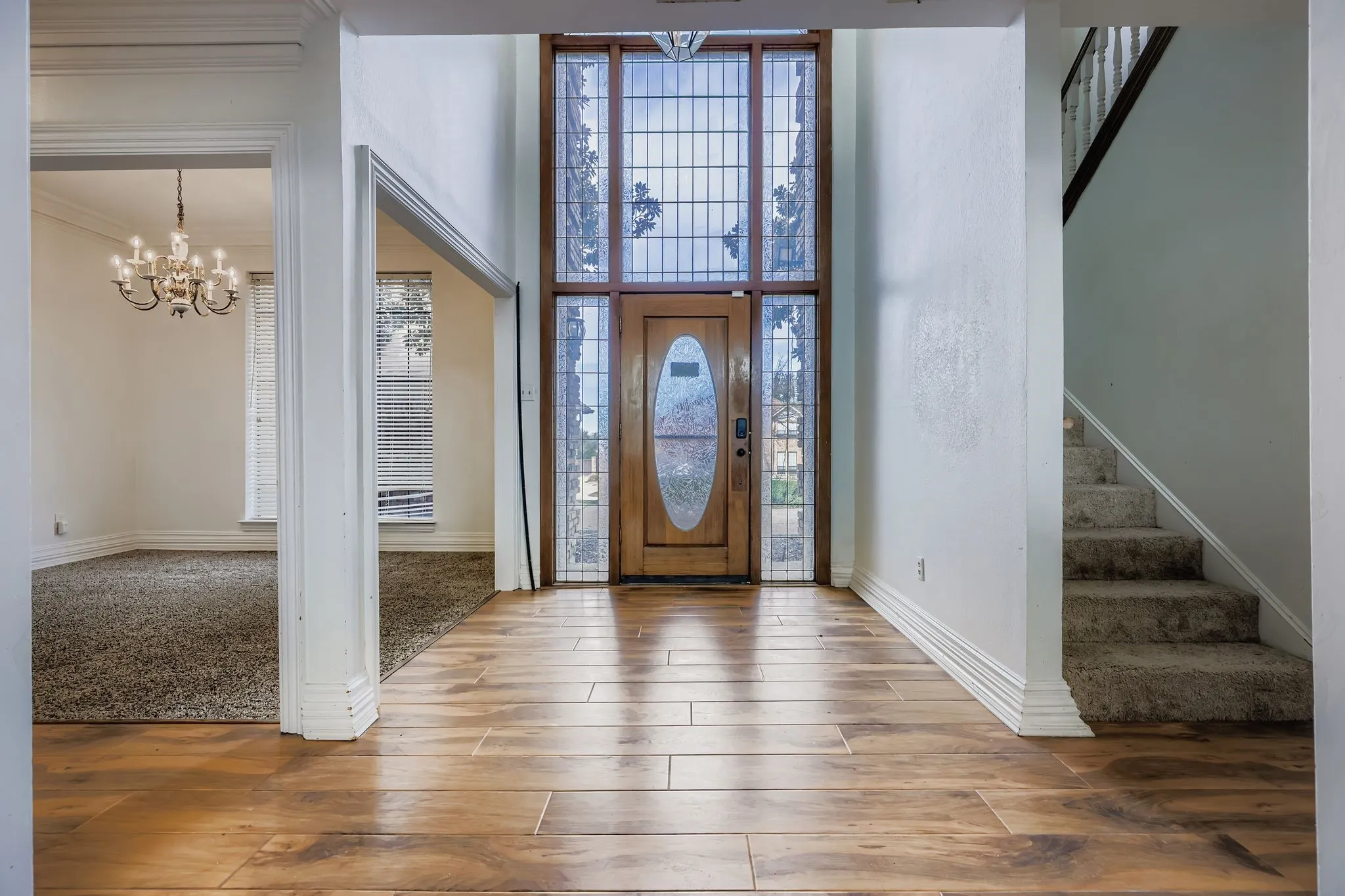 Two-story foyer featuring wood-finish flooring, a wood entry door with oval glass inset, and a full-height sidelight with decorative leaded glass