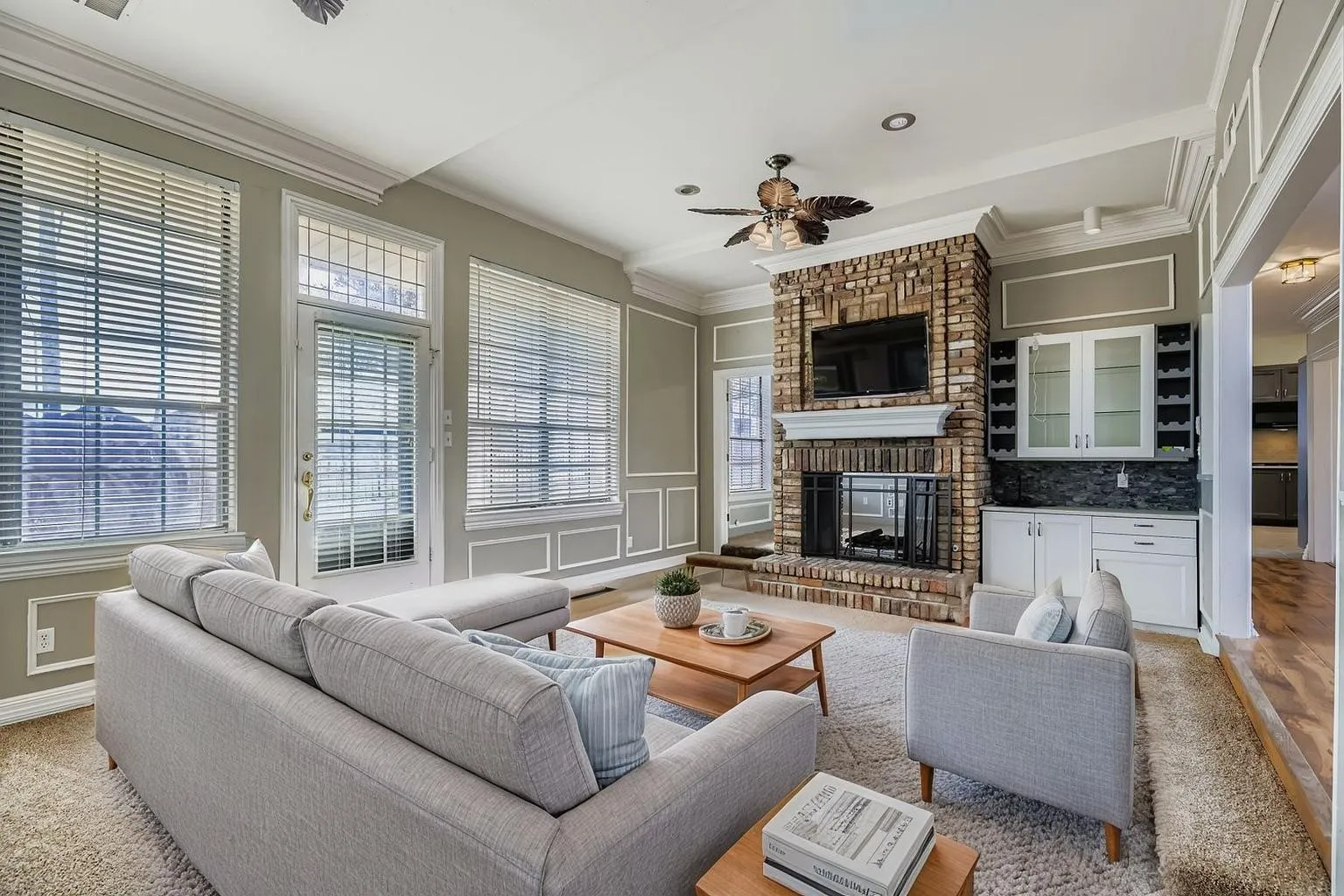 Brick fireplace with a substantial hearth, built-in wet bar featuring upper glass-front cabinetry, multiple windows, and crown molding