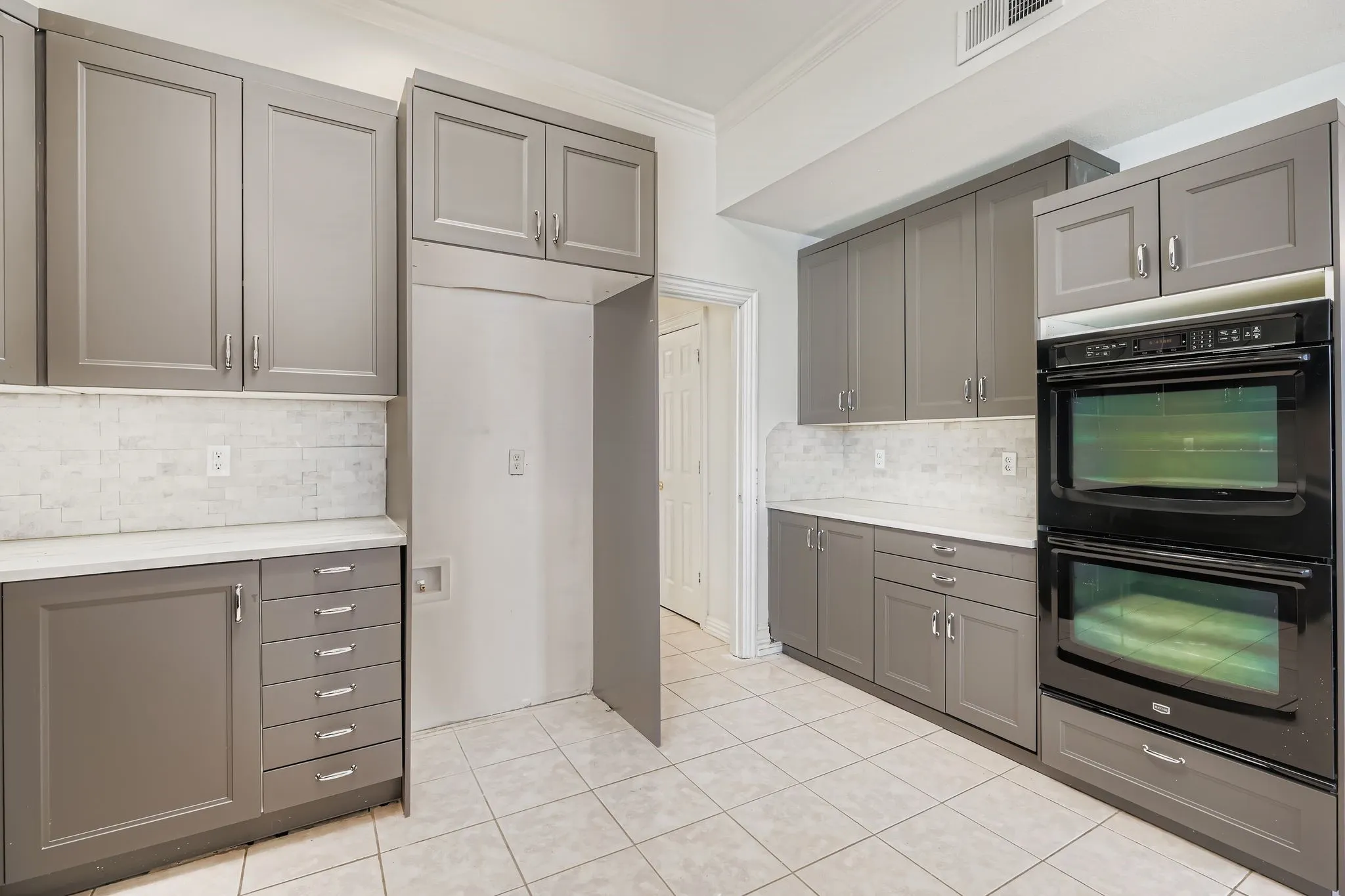 Contemporary cabinetry with a neutral finish, white countertops, dual built-in ovens, and a tile backsplash