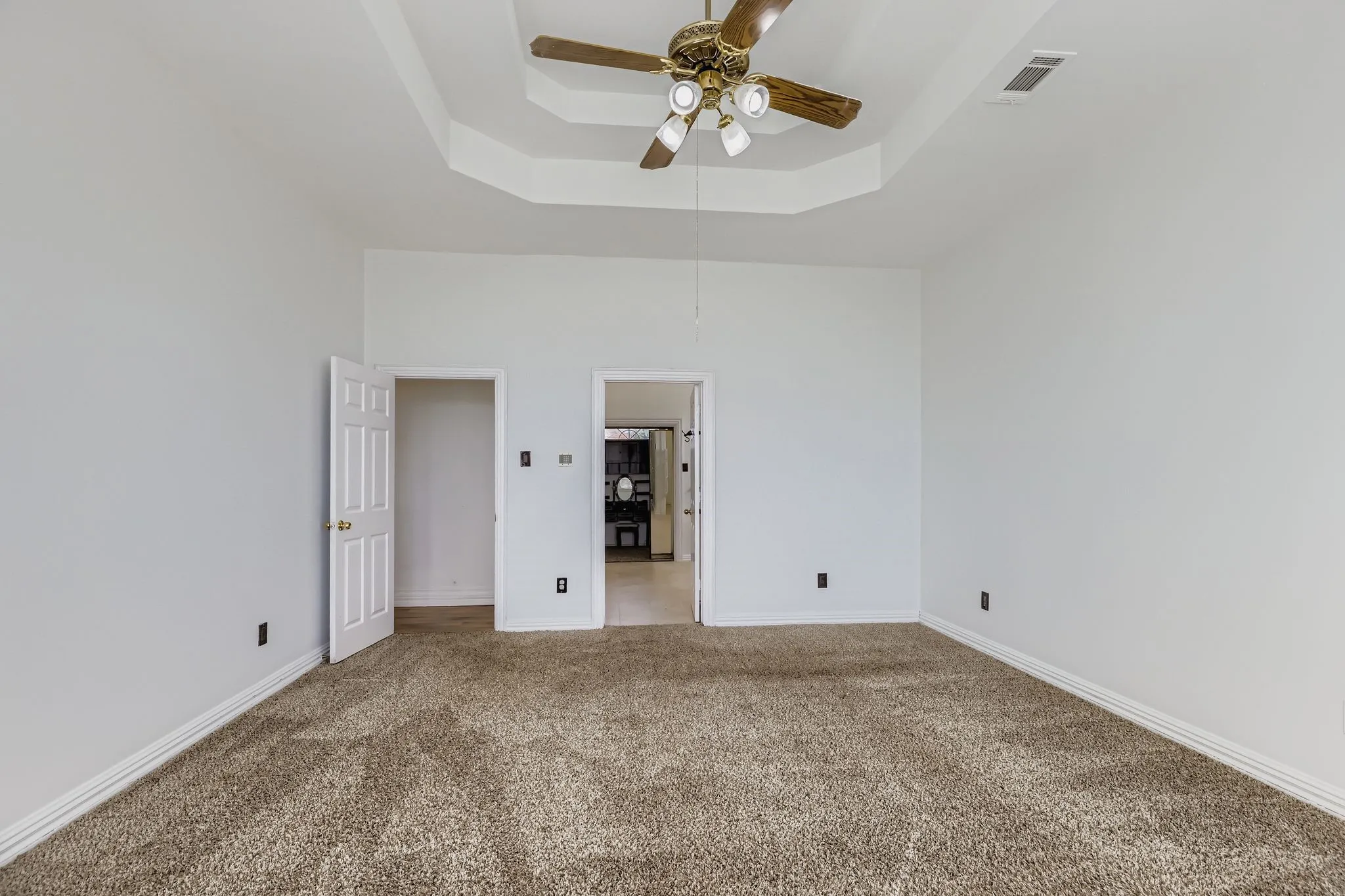 Recessed tray ceiling with a built-in ceiling fan, neutral wall paint, and plush carpeting