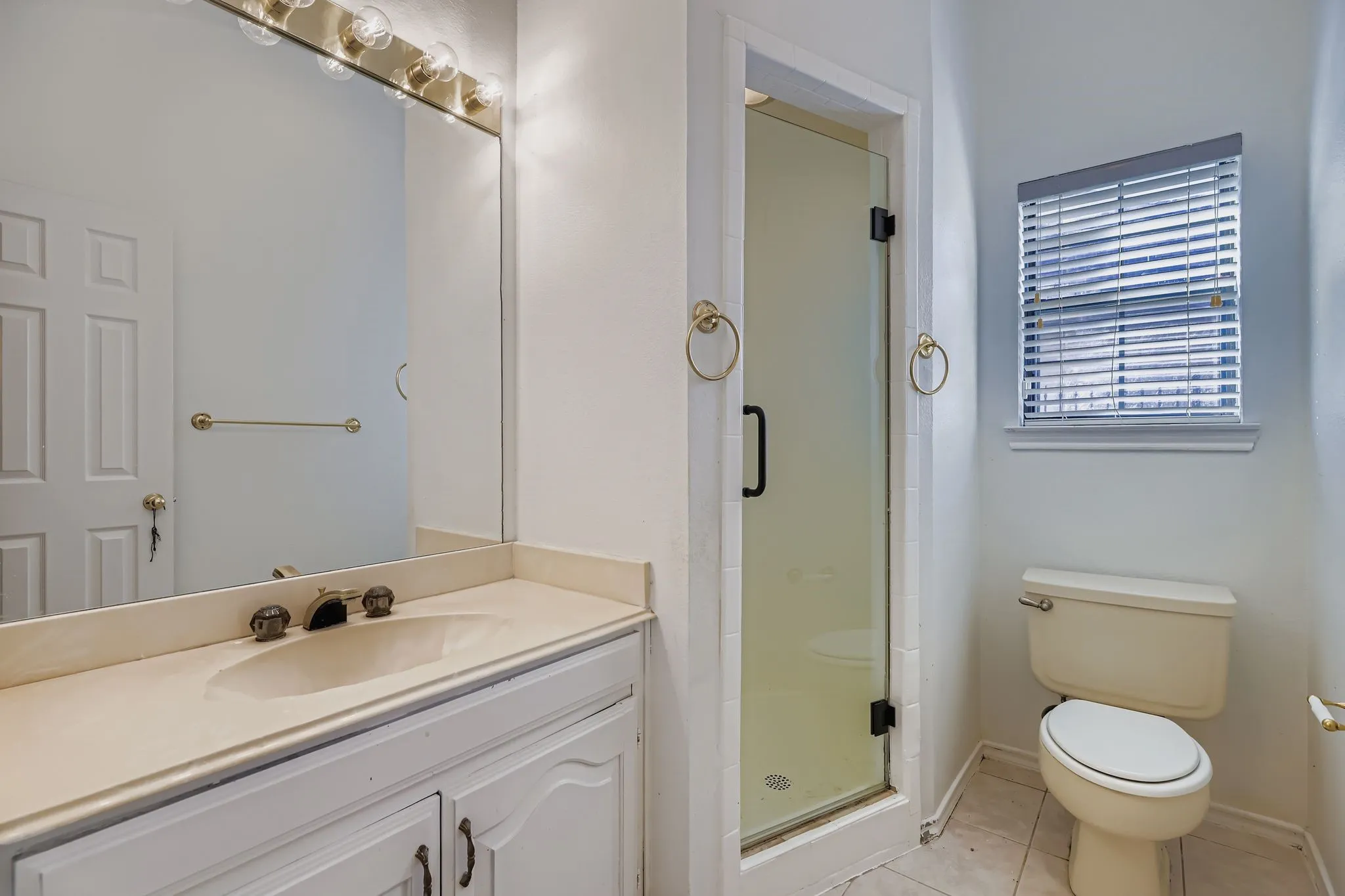 Vanity with an integrated sink and base cabinetry, glass-enclosed shower, and a window with blinds