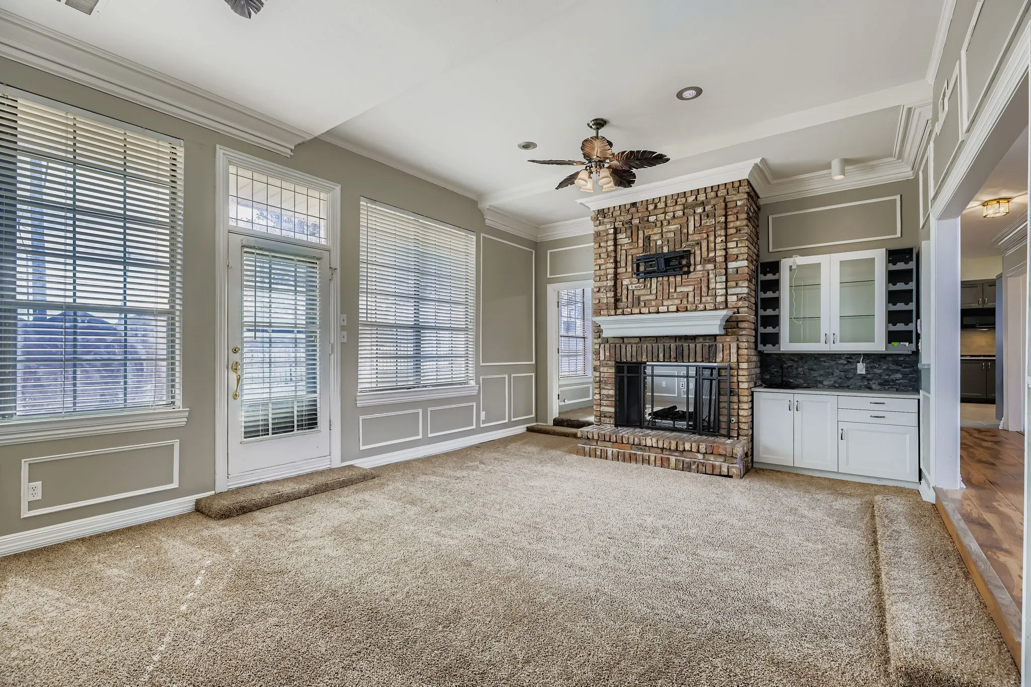 Brick fireplace with an integrated mantel, built-in cabinetry with glass-front uppers, crown molding, and recessed lighting